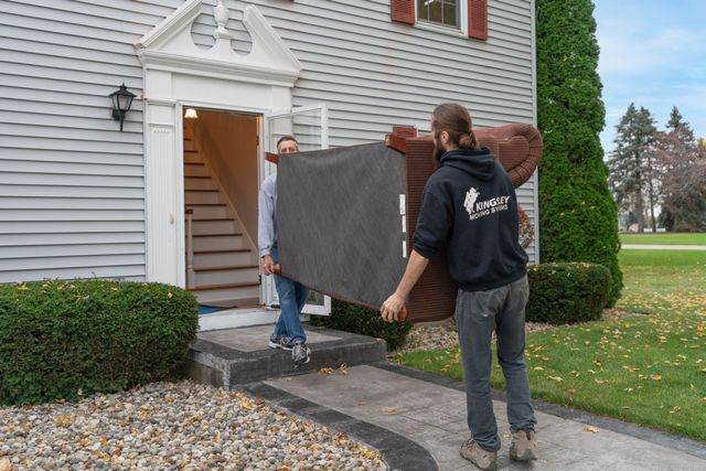 Three people carrying a large dark panel into a house through the front door