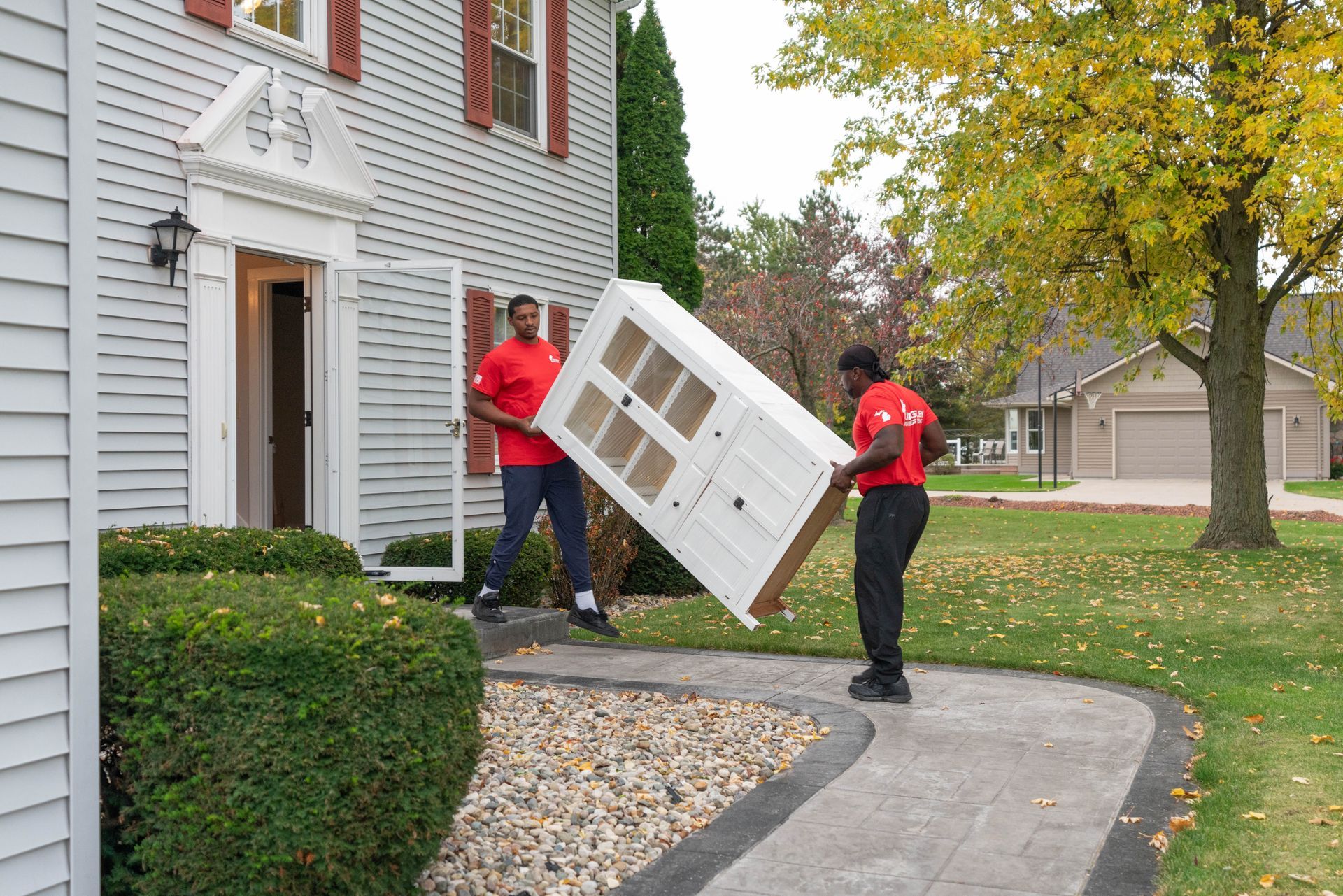 Two movers carrying a white cabinet up a front walkway to a house