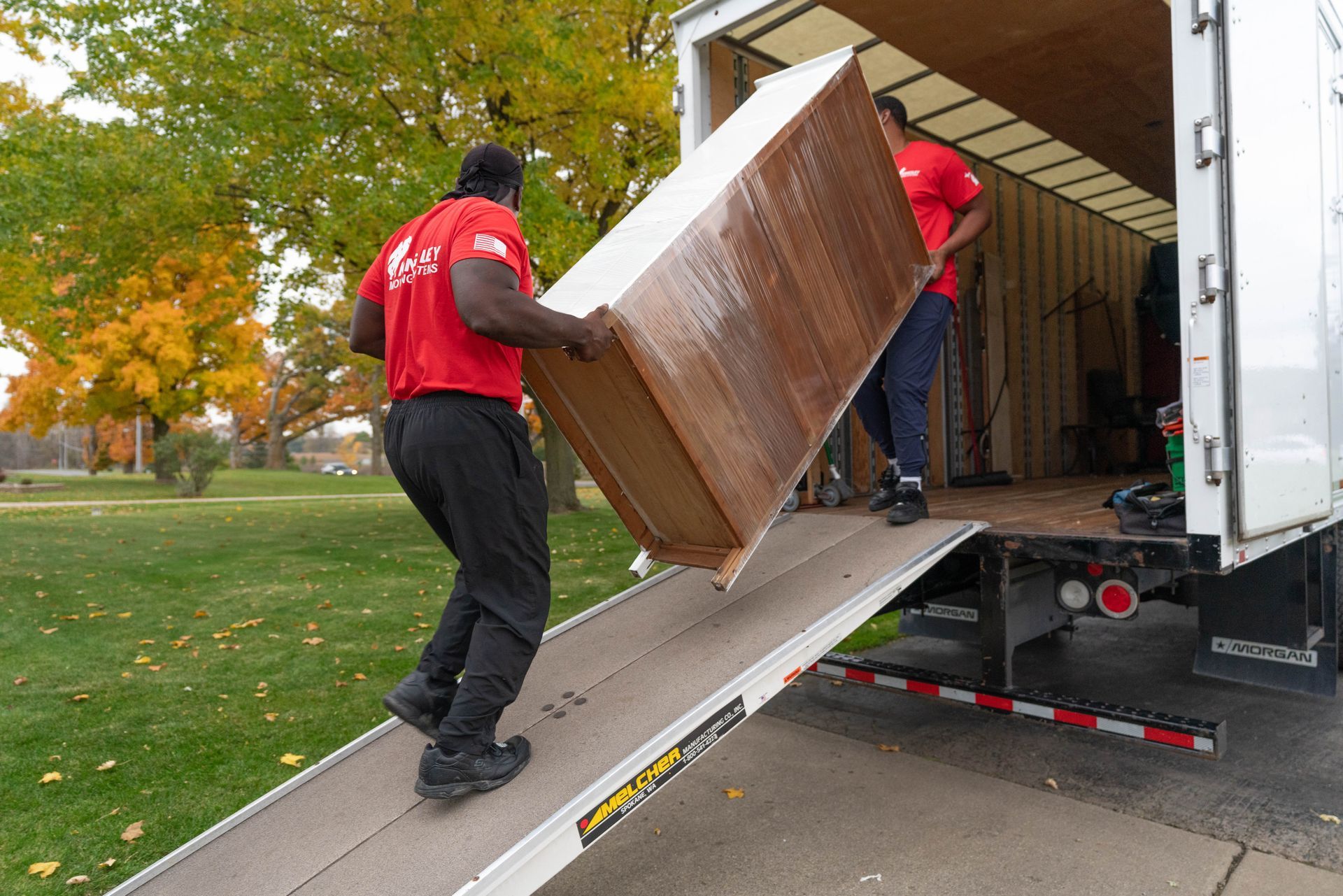 Movers loading a large wooden dresser up a ramp into a moving truck