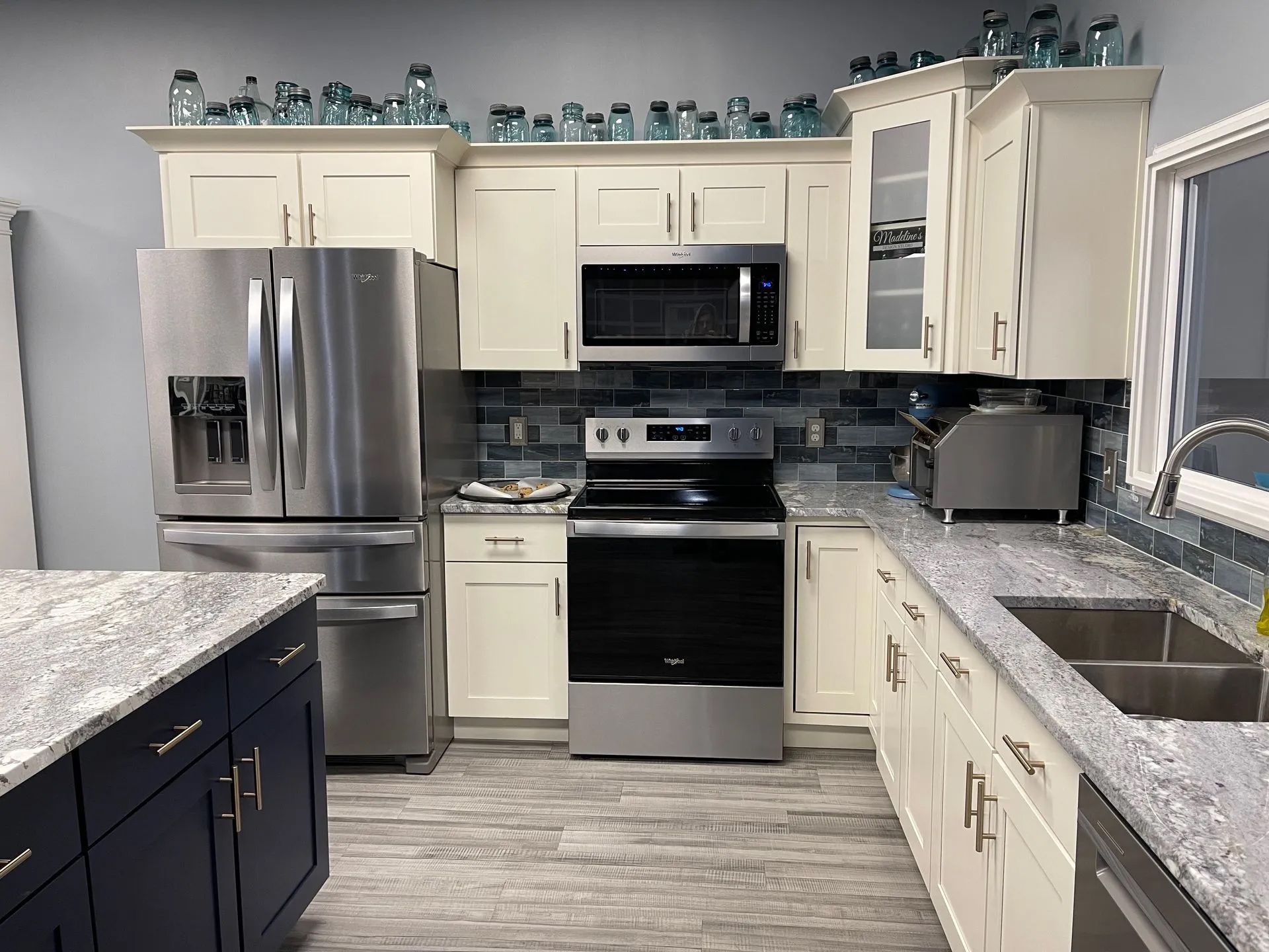 Modern kitchen with stainless steel appliances, blue backsplash, and light countertops.