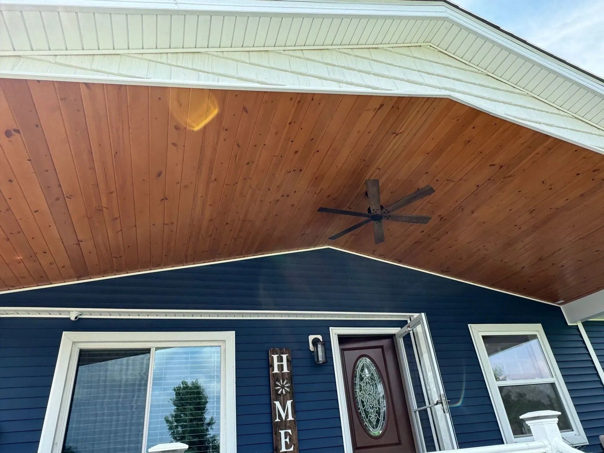 Blue house with a brown wood porch ceiling, a ceiling fan, and a front door