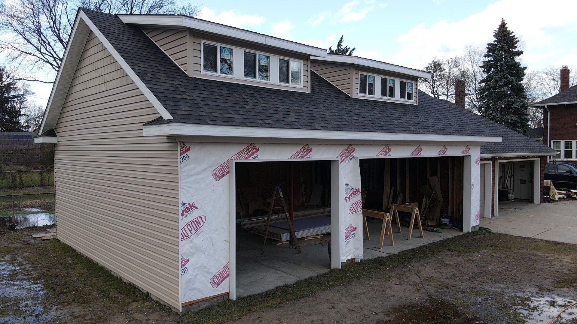 Two-story garage under construction with beige siding, black roof, and three garage door openings.