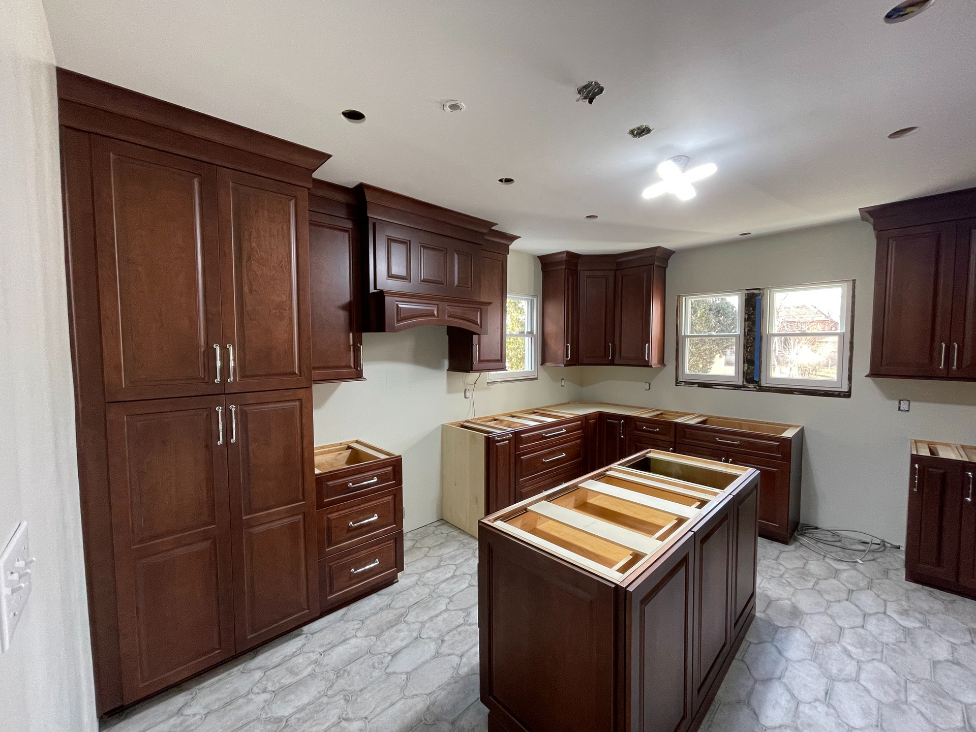 Newly installed dark brown kitchen cabinets in a room with gray and white tile flooring.