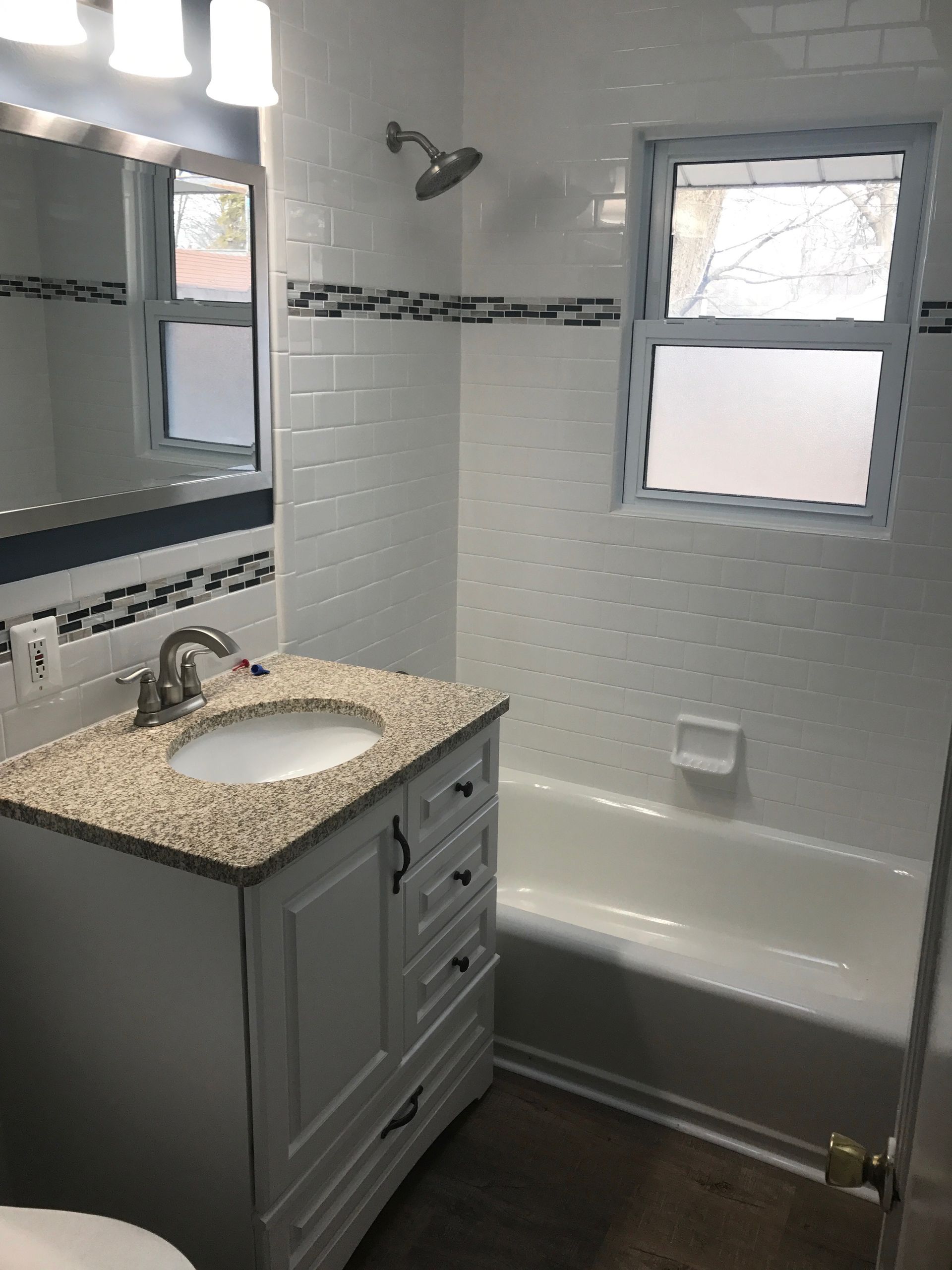 White bathroom with a vanity, bathtub, shower, and a small window.