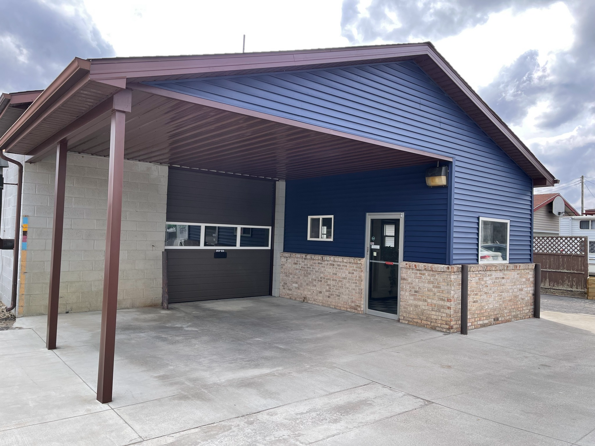 Blue building with brown awning and garage door, concrete area, and brick trim.