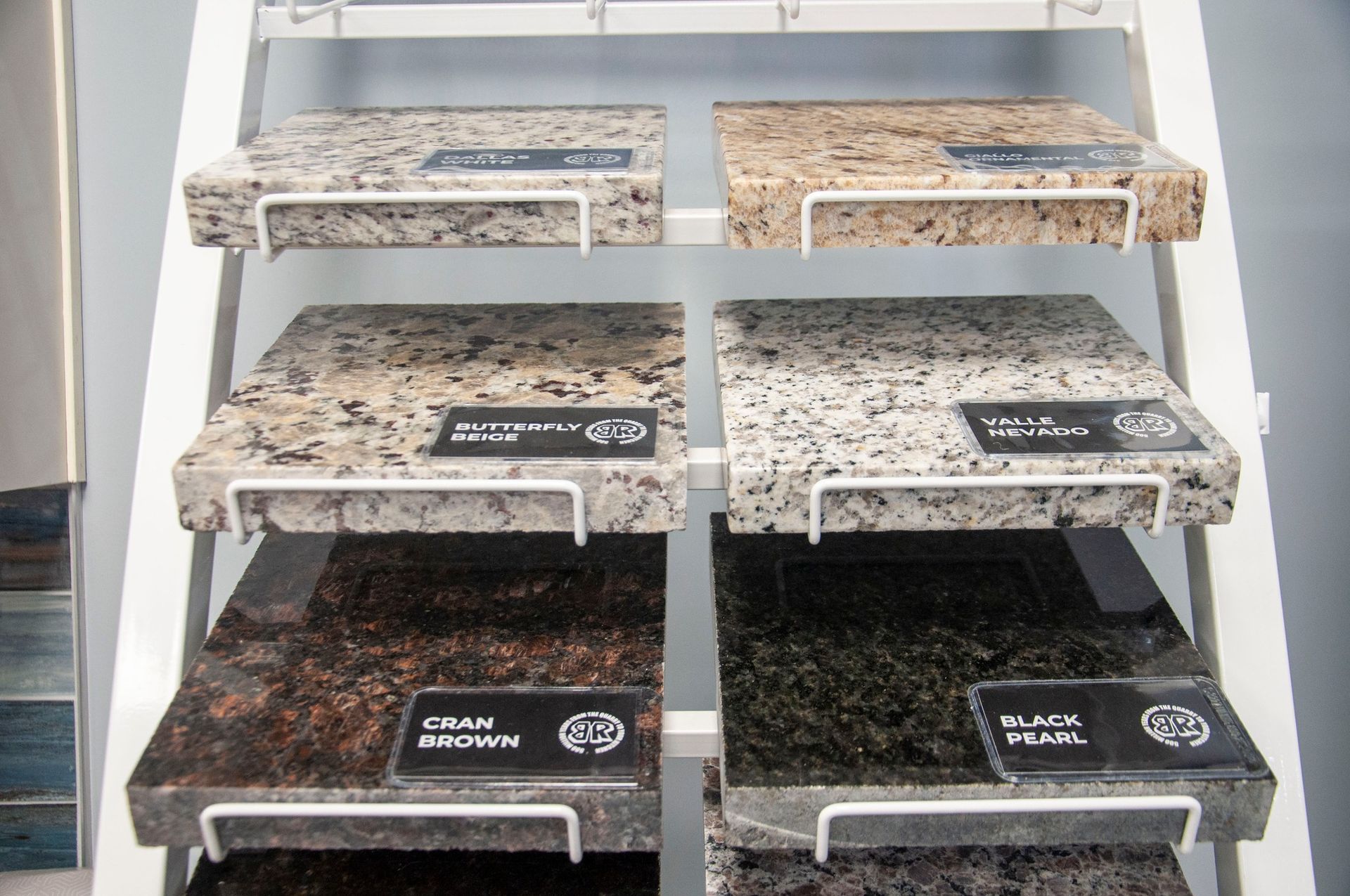 Display of granite countertop samples on a tiered, white metal rack.