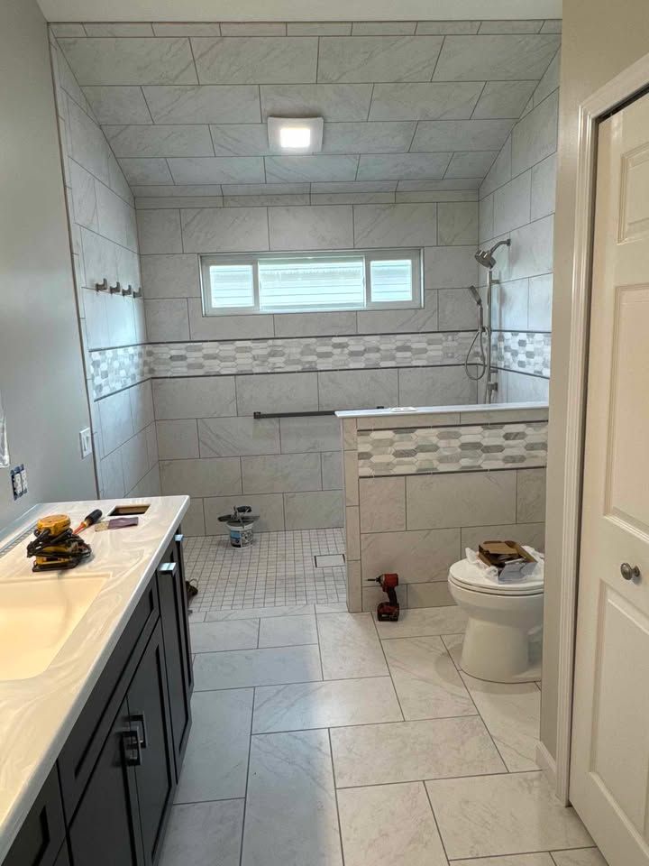 Bathroom with tiled shower and vanity, accessible design with grab bar. White and gray tones.