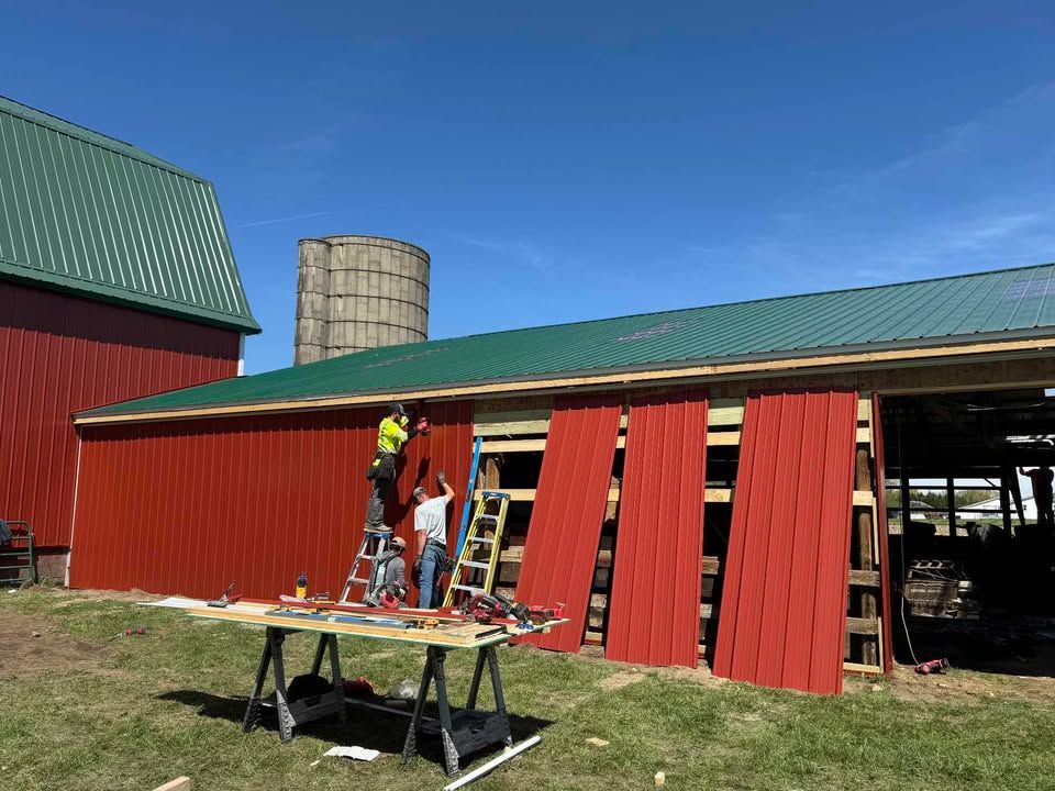 Two people building a red barn with green roof on a sunny day.