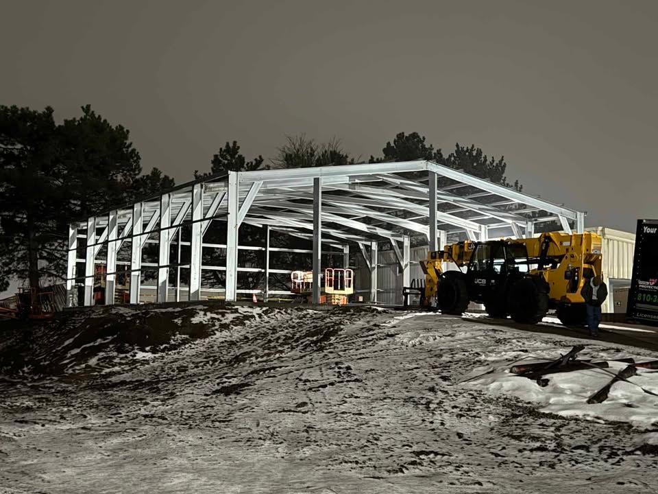 Steel frame construction of a building at night, with a forklift on the snowy ground.
