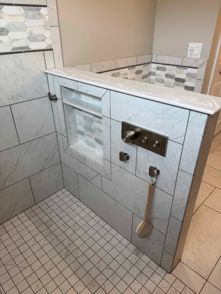 Shower with white marble tiles and a built-in shelf, showerhead, and body brush hanging.