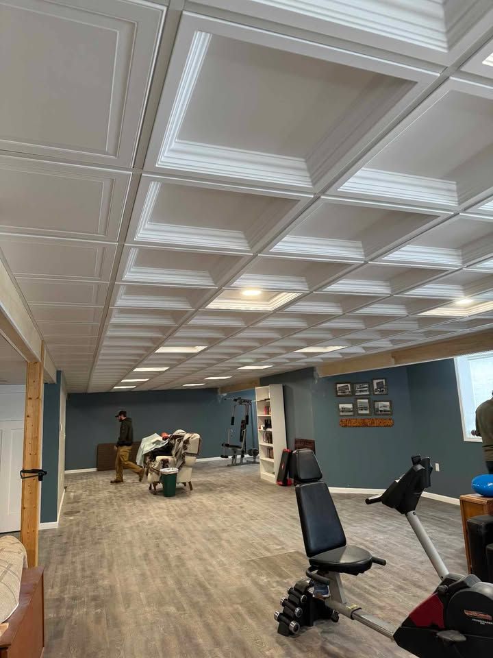 Basement gym with wood-look flooring, exercise equipment, a person, and a patterned ceiling with recessed lighting.