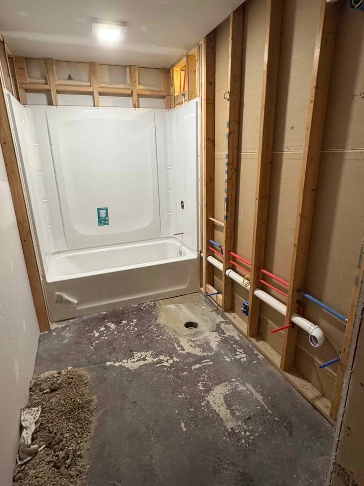 Bathroom under construction with a white tub, exposed framing, and plumbing.