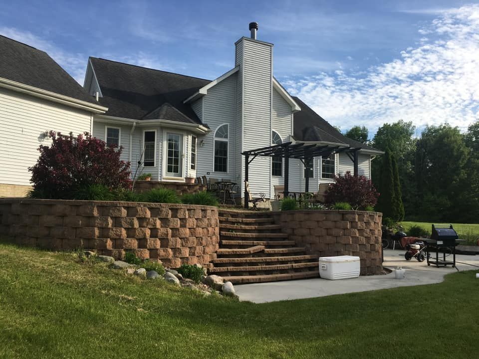 Stone steps lead up to a house with a pergola and chimney, with a retaining wall and sunny sky.