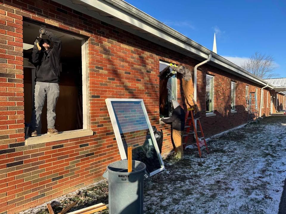 Workers removing windows from a brick building. Snow on the ground.