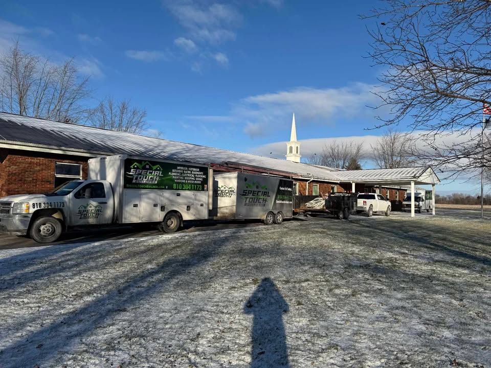 Trucks parked in front of a building with a snow-covered roof; a church steeple is in the background.