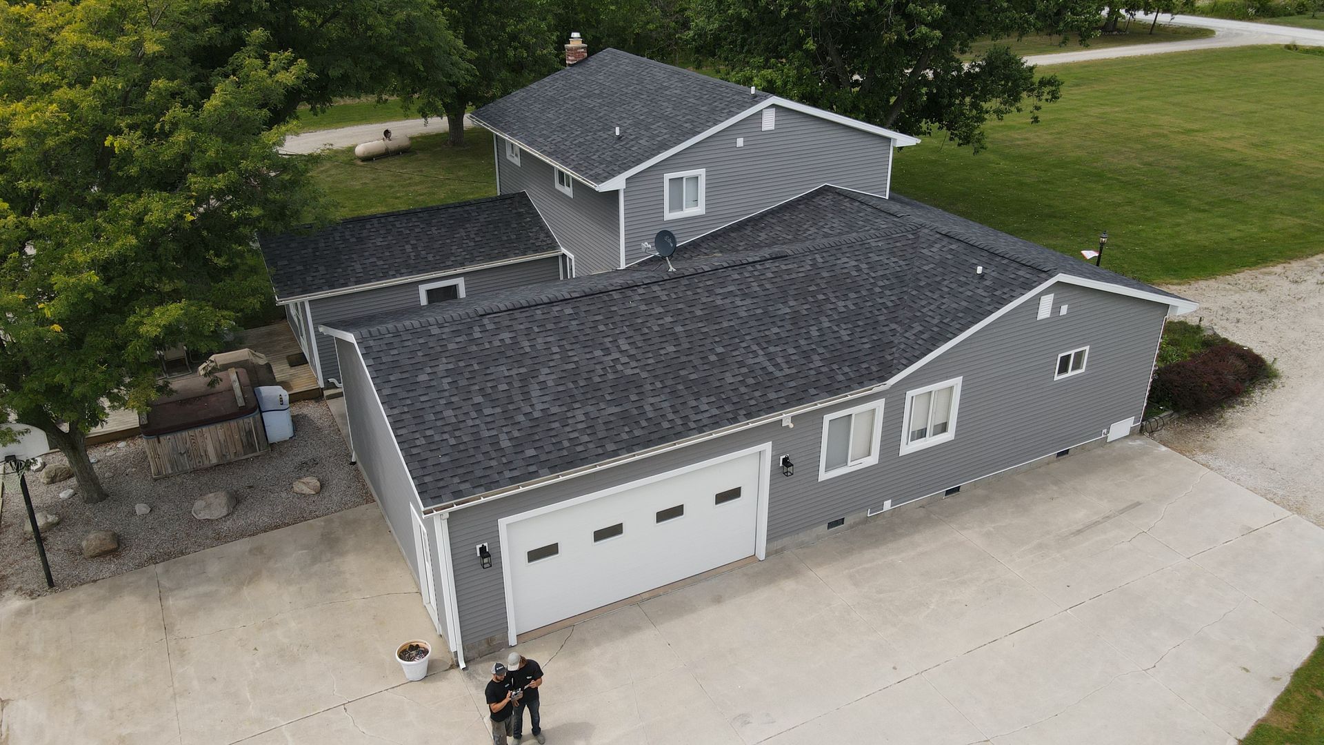 Gray house with attached garage, two people standing in front on a concrete driveway.
