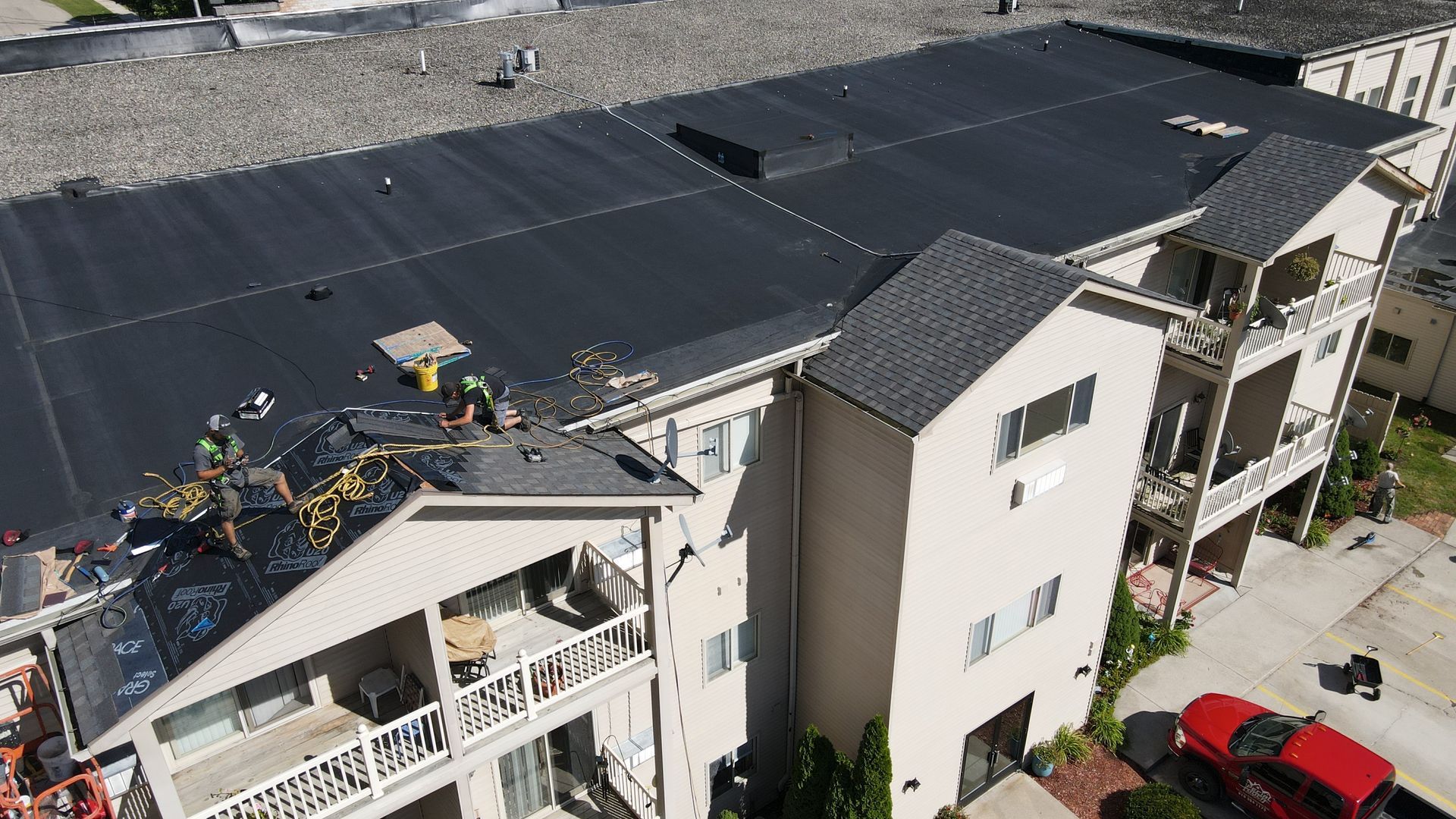 Building with a black flat roof under construction; workers on roof.
