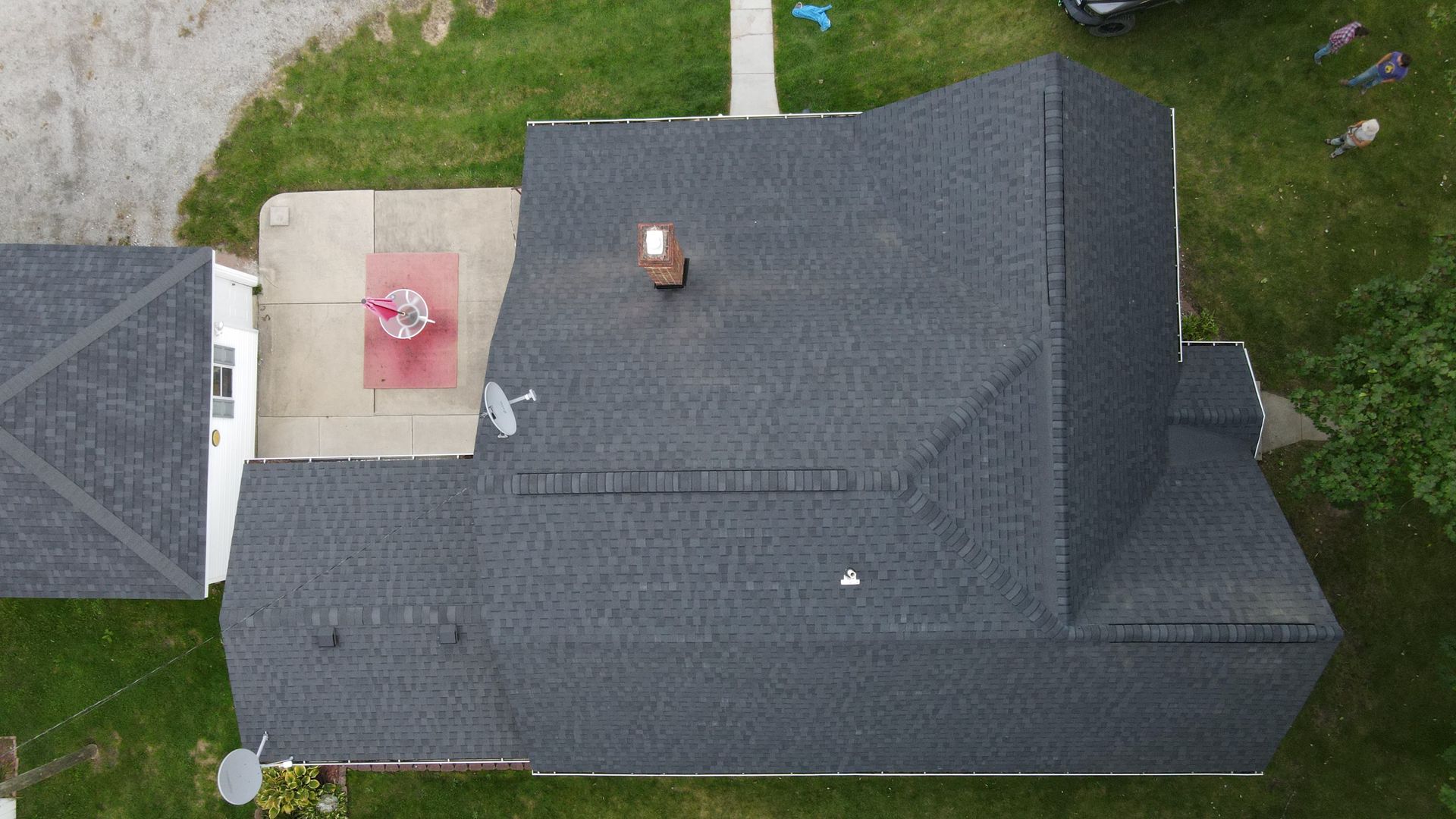 Overhead view of a house with a dark gray roof, chimney, and satellite dish on a green lawn.