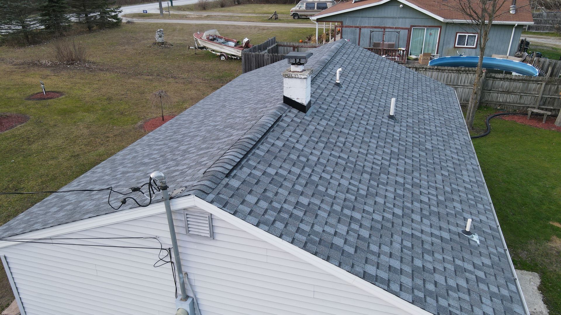 Overhead view of a house with a gray shingle roof and white chimney. Green grass surrounds it.
