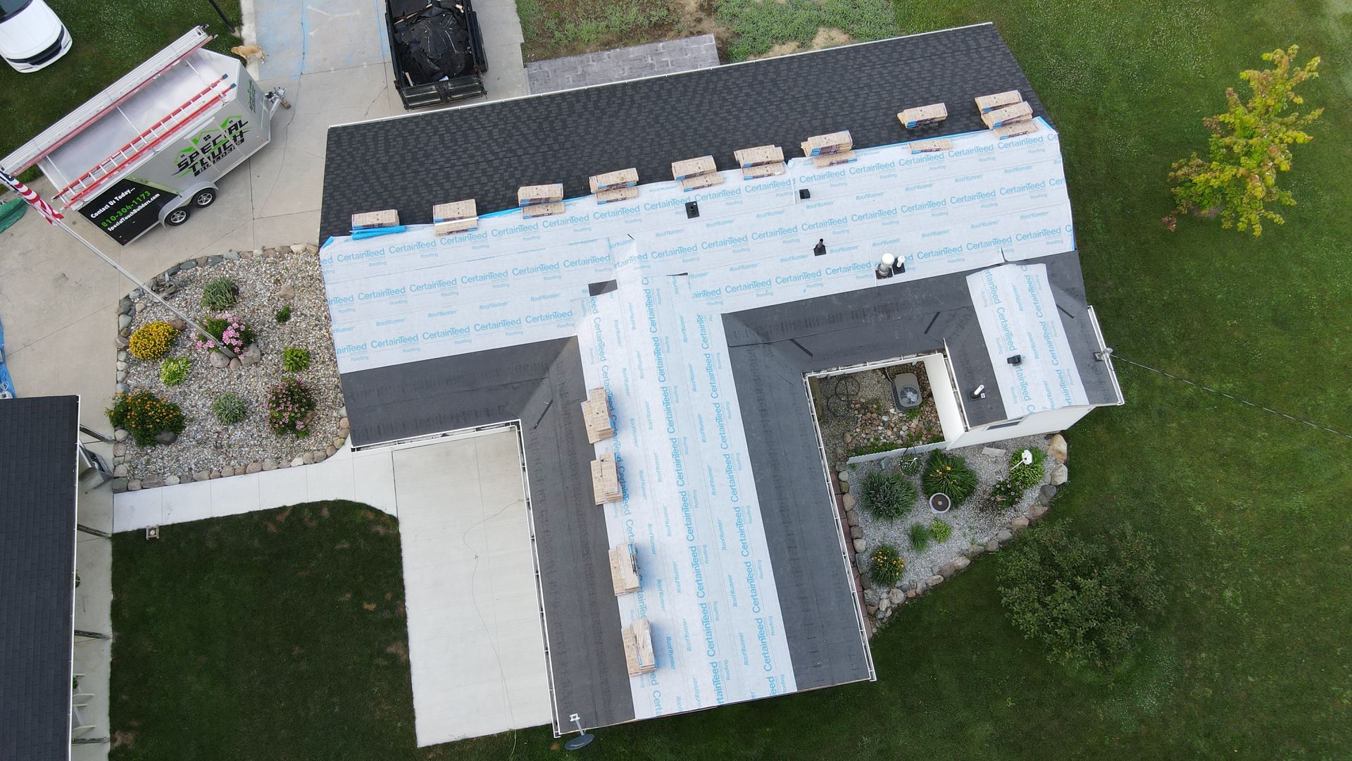 Aerial view of a house roof partially covered with dark shingles and white underlayment, construction in progress.