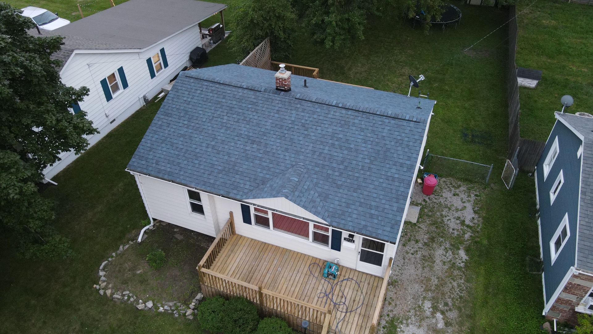 An aerial view of a small white house with a blue roof and wooden deck.