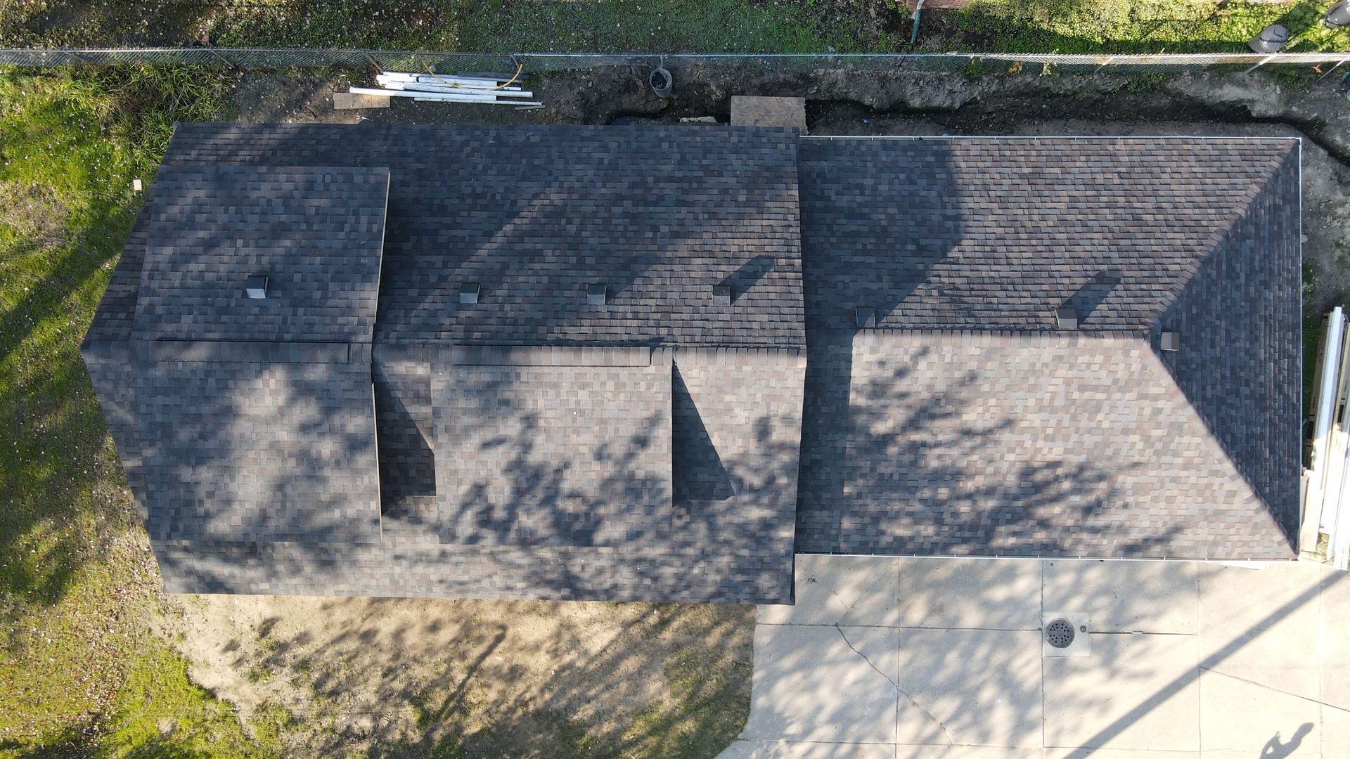 Overhead view of a house roof with dark shingles. The house is surrounded by a yard and driveway.