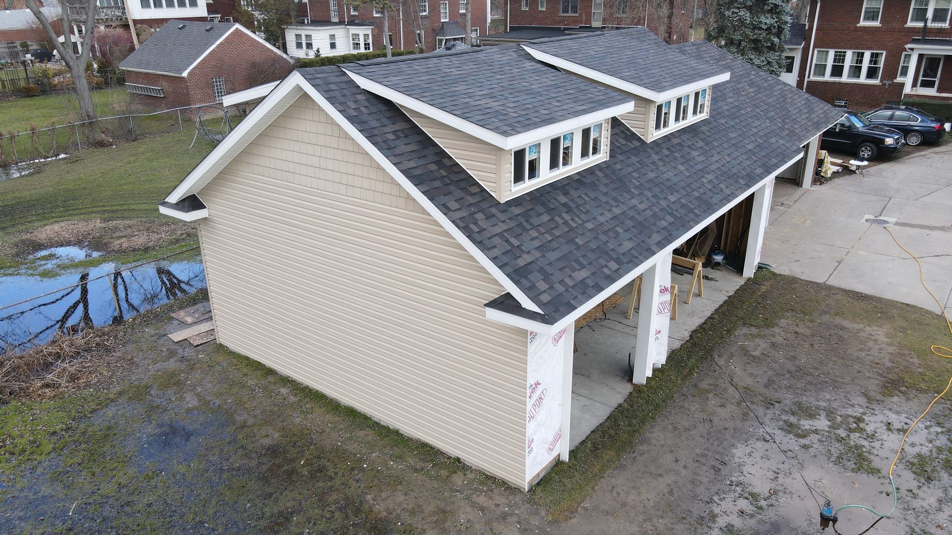 Tan garage with a dark gray roof, two dormers, and open bays.