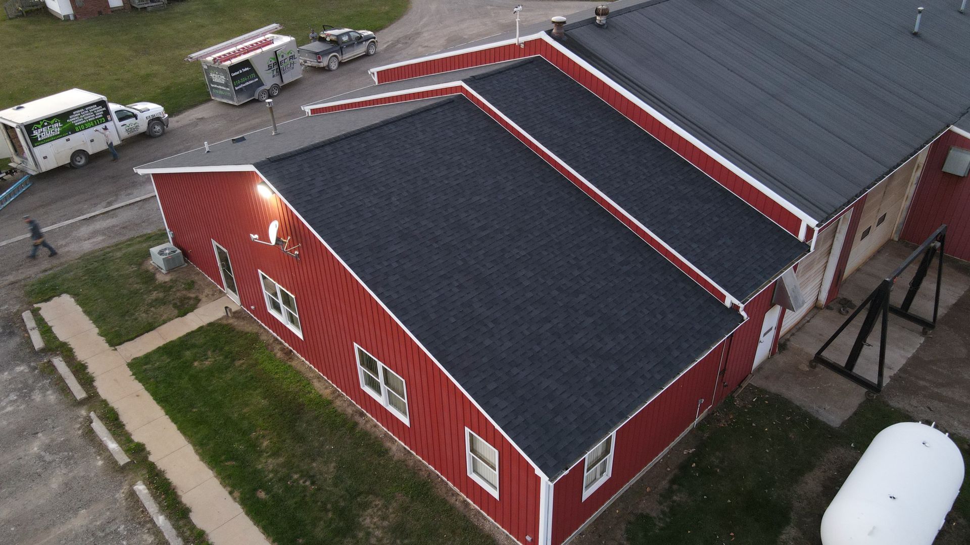 Aerial view of a red building with a black roof, windows, and a white trim. A person walks near a green lawn.