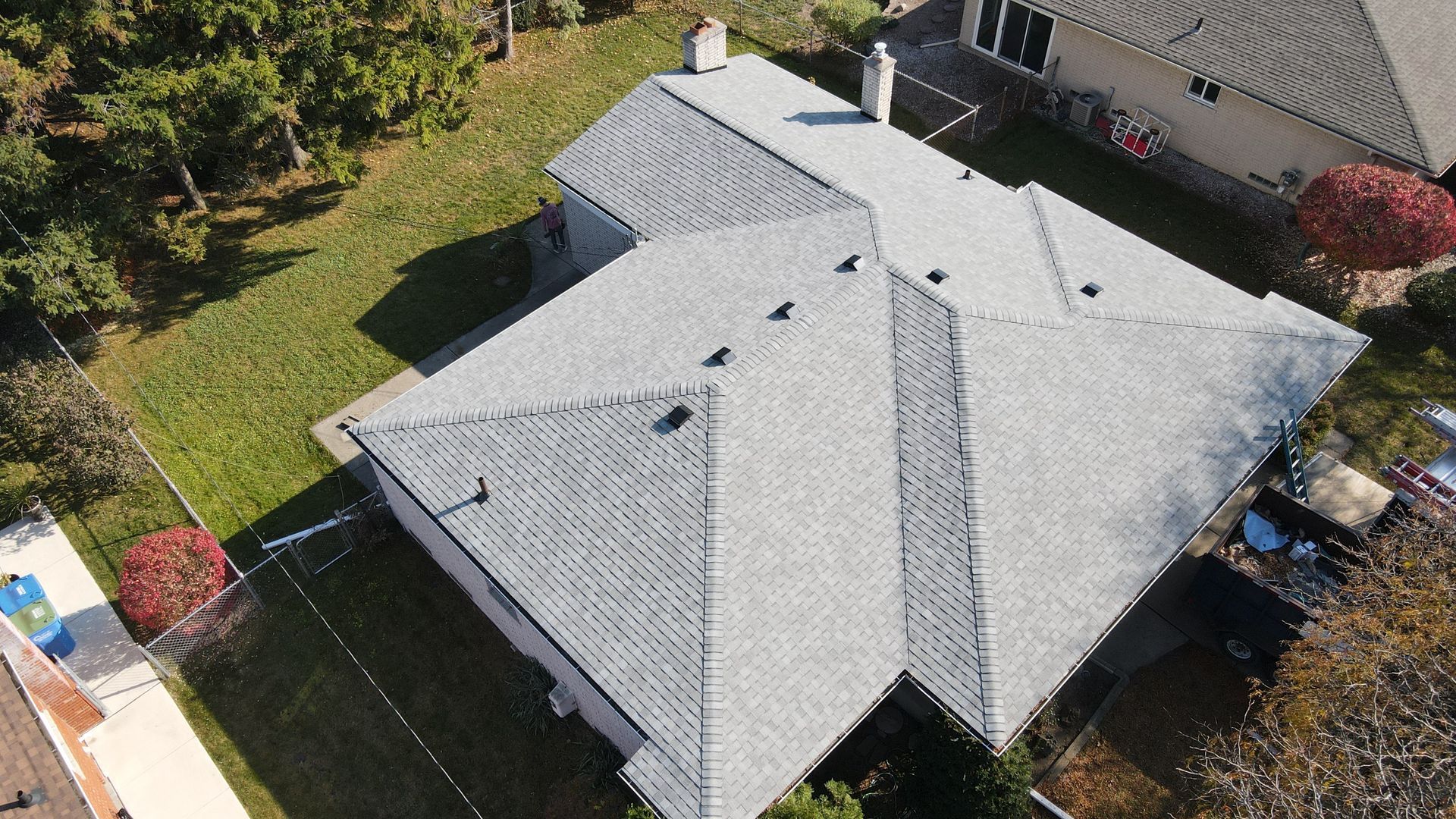 Gray shingle roof of a house with chimney, on green lawn. Aerial view.