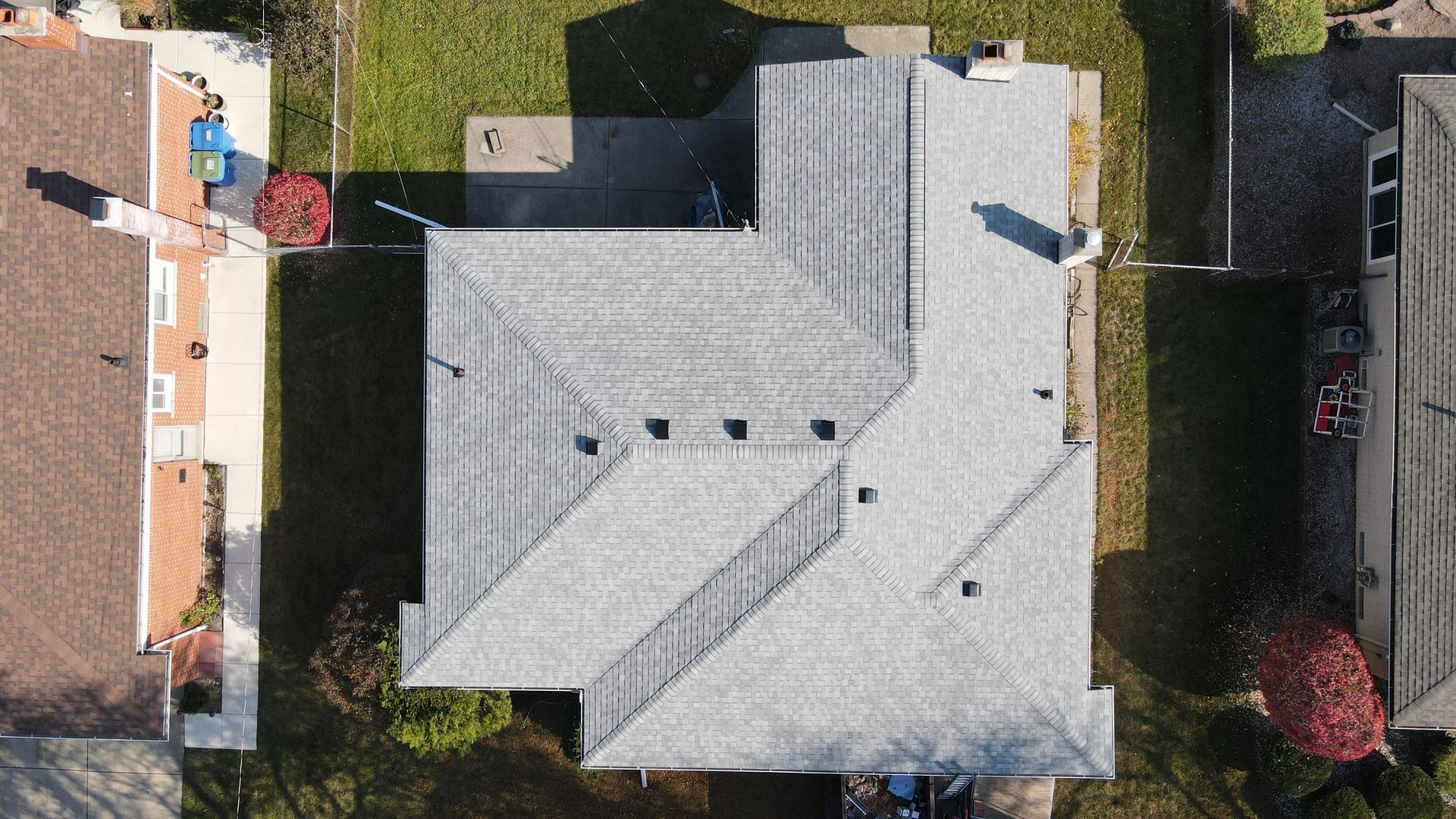 Aerial view of a gray-roofed house with a yard and surrounding houses.