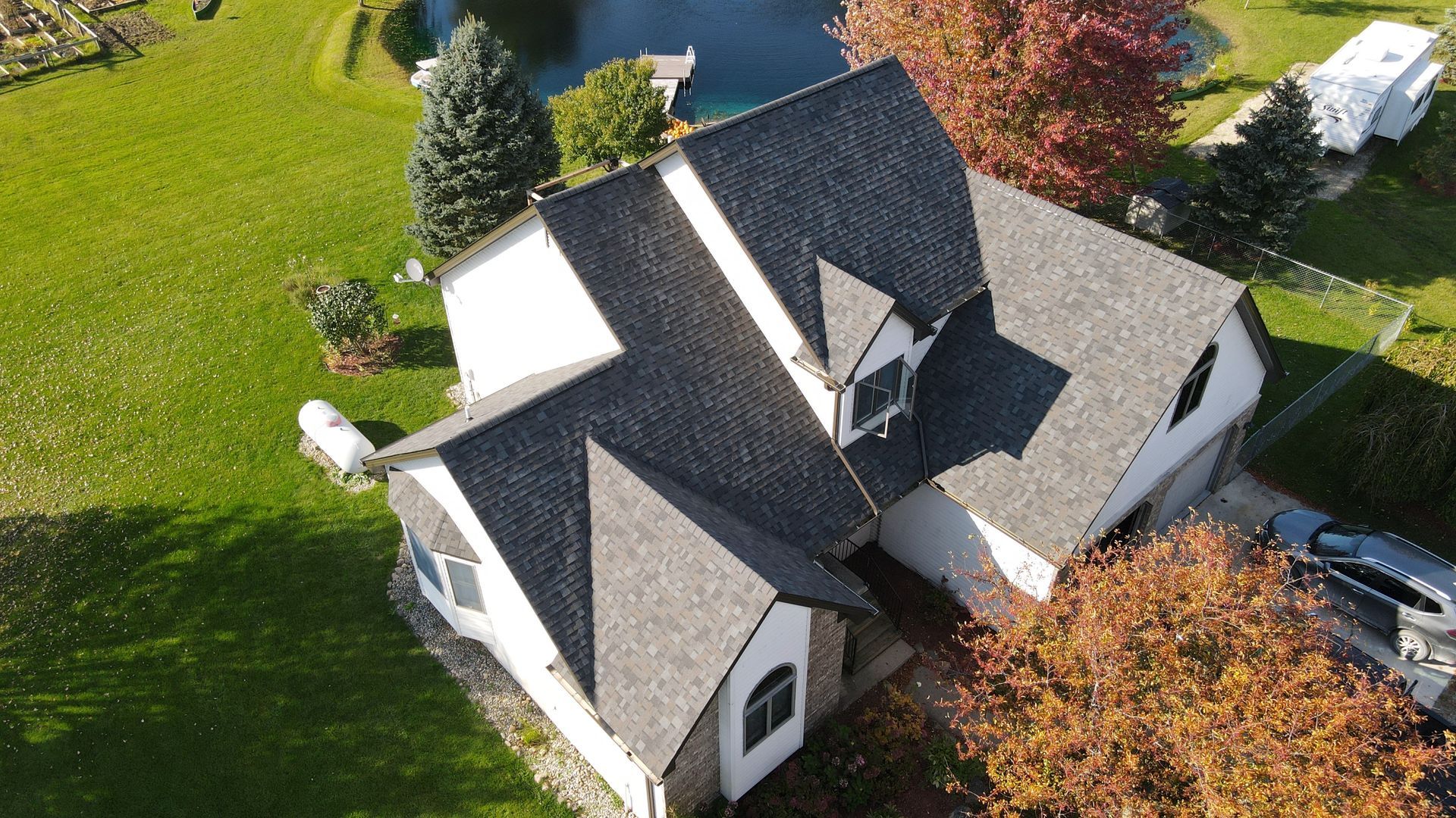 Aerial view of a house with a dark roof and white siding, near a lake with fall foliage.