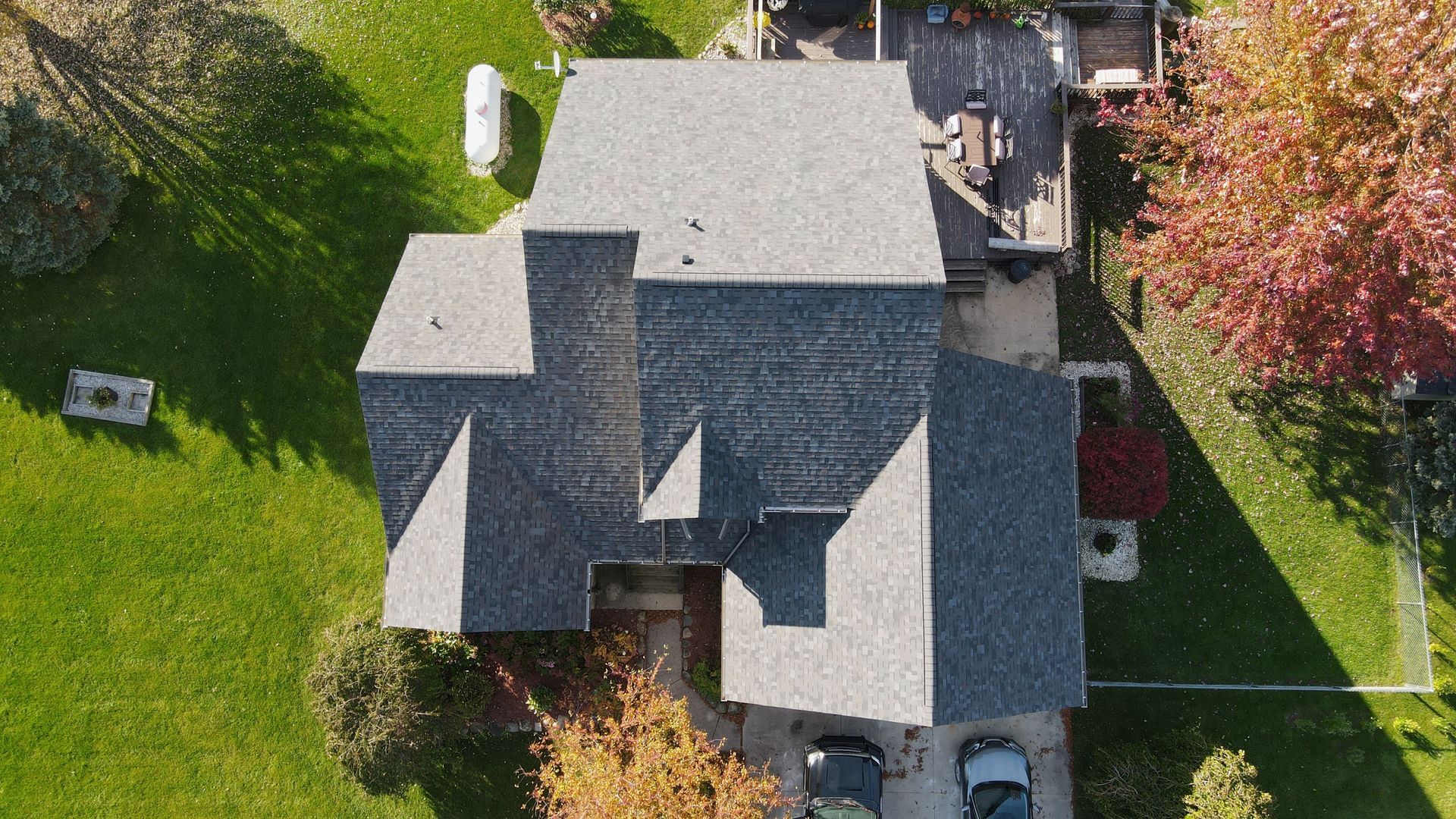 Overhead view of a house with a gray roof and a green lawn, next to a deck and colorful trees.