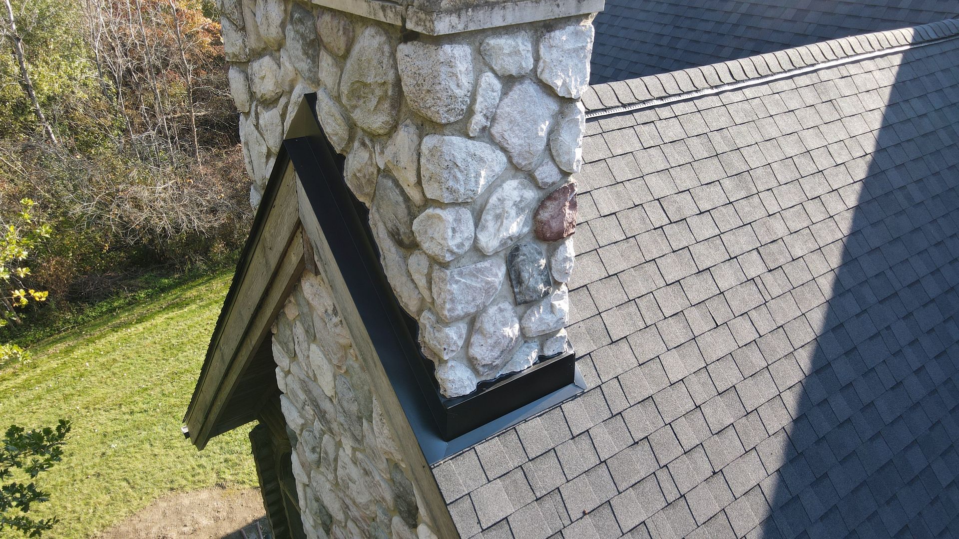 Stone chimney on a shingled roof with dark flashing; exterior shot.
