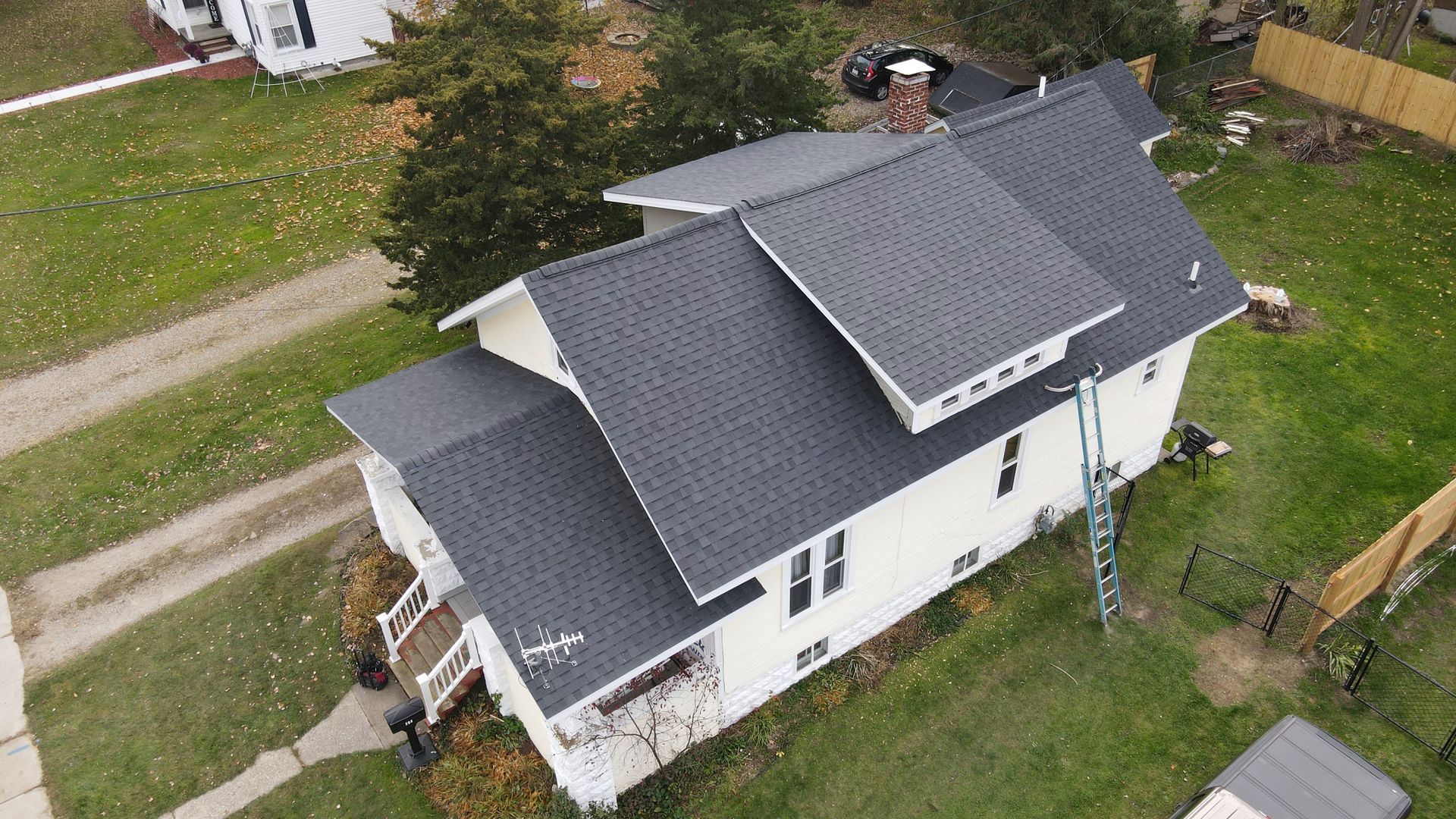 Aerial view of a white house with a dark gray roof. A ladder is leaning against the side.