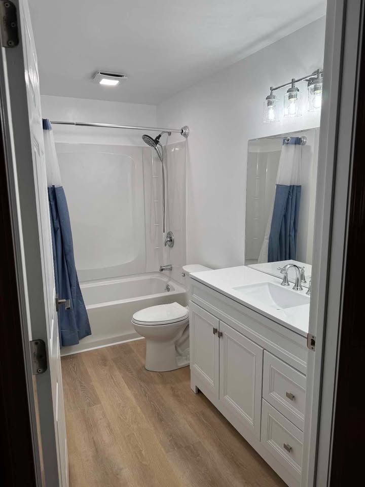 Bathroom with white walls, vanity, and tub, light wood-look flooring. Blue shower curtain.