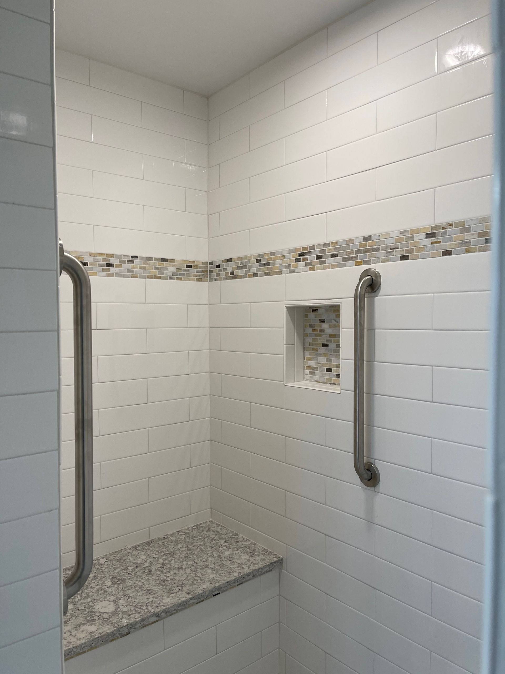 Accessible white-tiled shower with a bench, grab bars, and pebble accent.