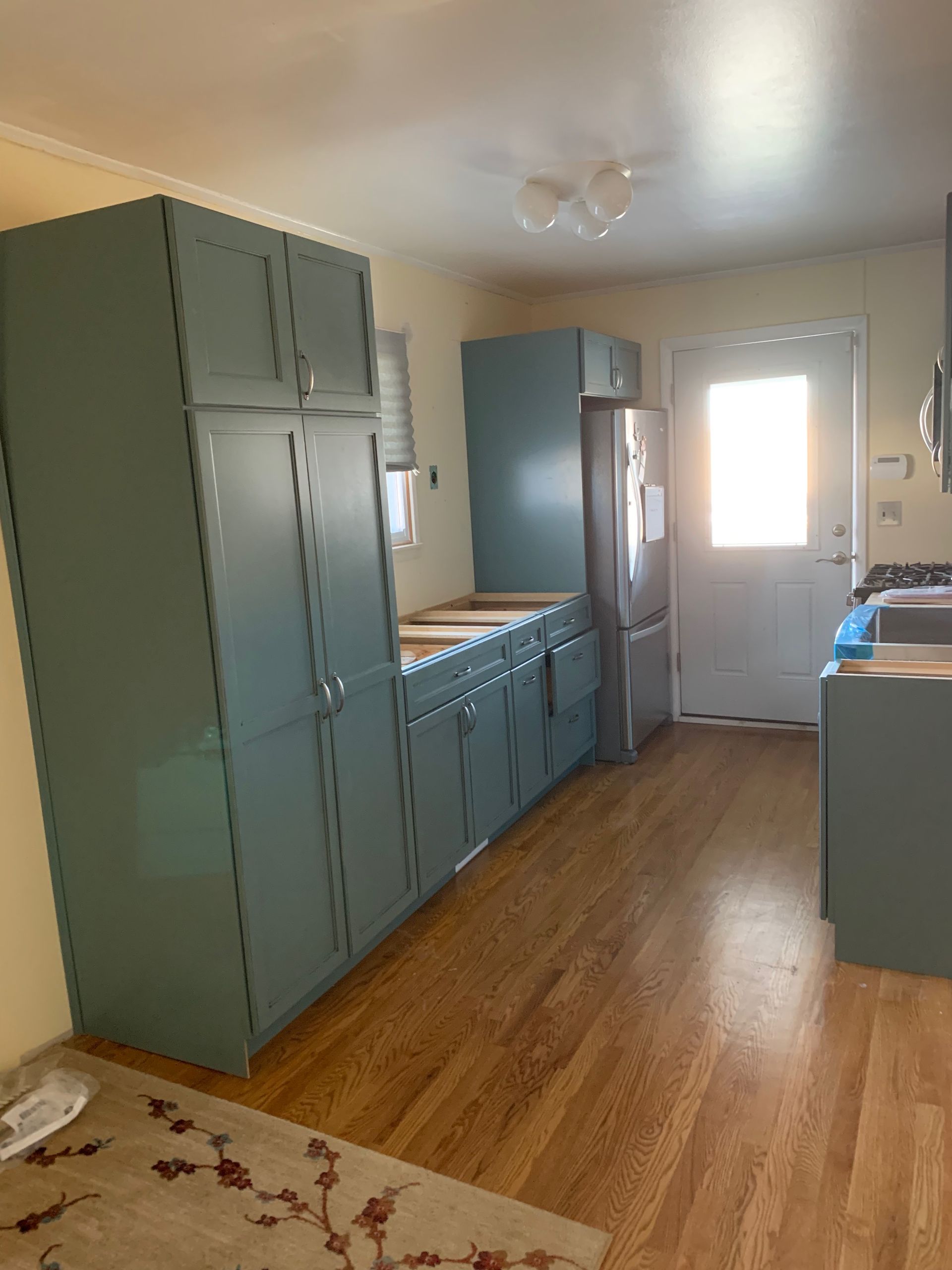 Kitchen with blue cabinets, a refrigerator, and a door, featuring wood flooring.