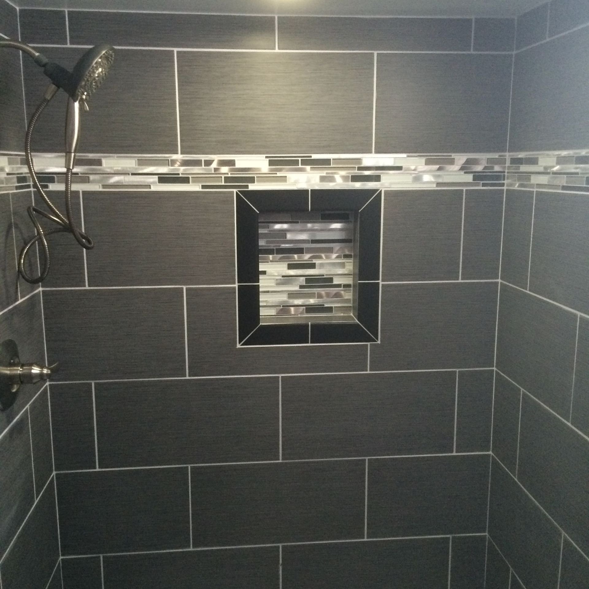 Dark gray tiled shower with a decorative mosaic tile strip and a built-in shelf.
