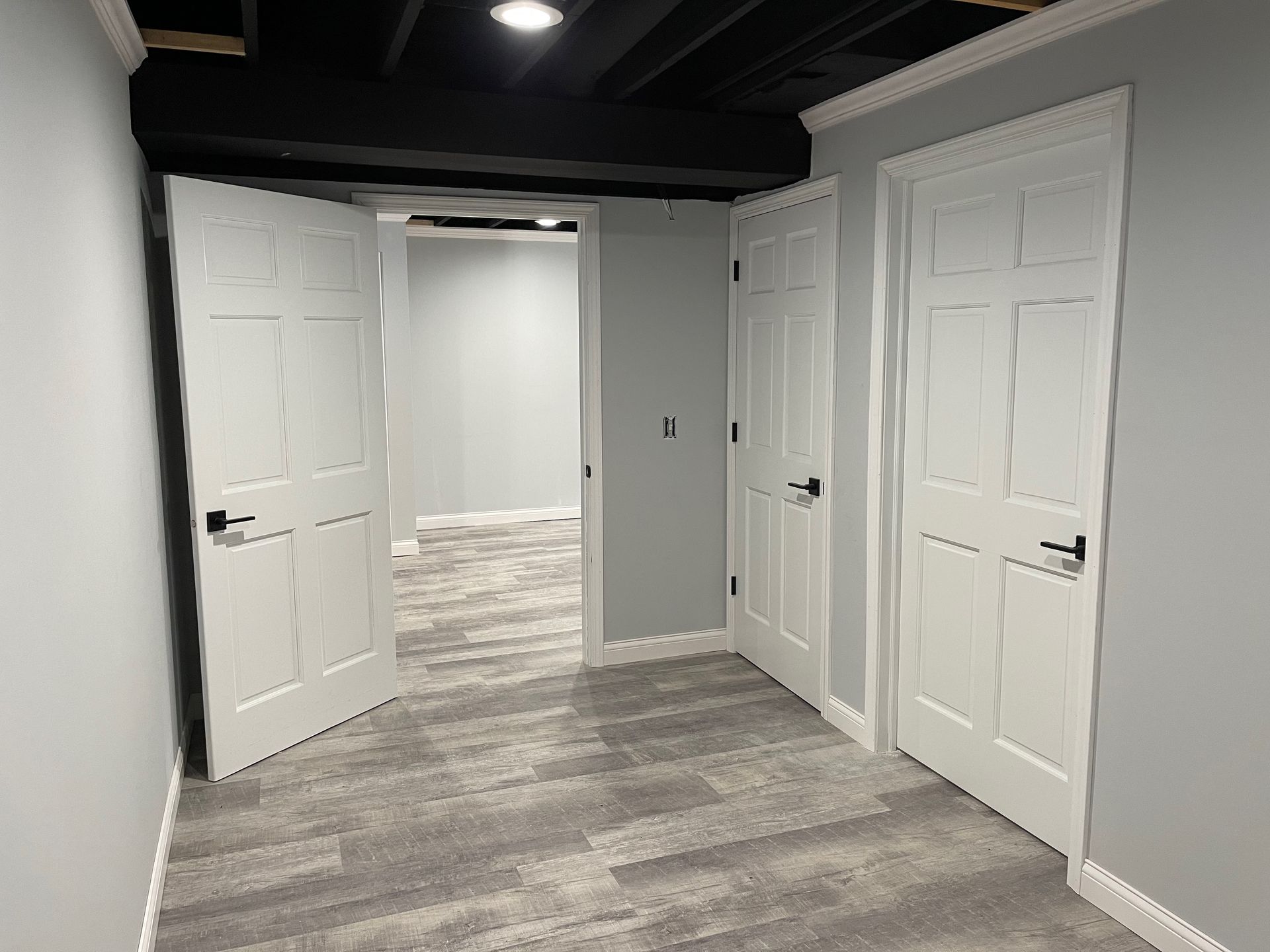 Interior view of a room with two white doors and an open doorway leading to another room. Gray walls, carpet.