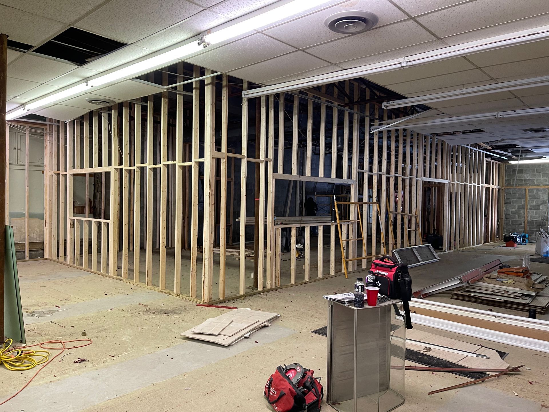 Interior construction site; wooden wall frames, windows, debris, tools on the floor.