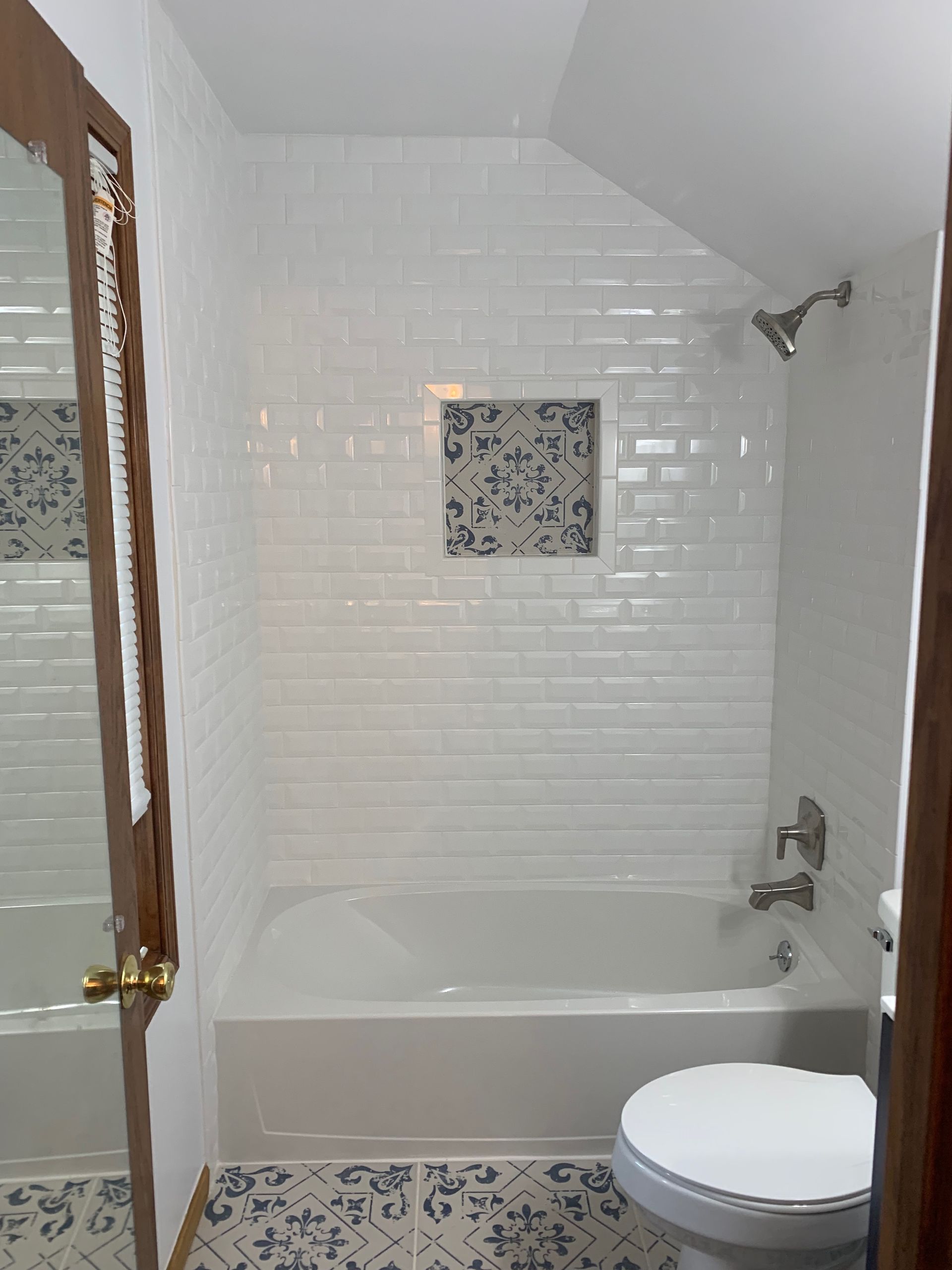 Bathroom with white subway tile shower, built-in shelf with decorative tile, bathtub, and toilet.
