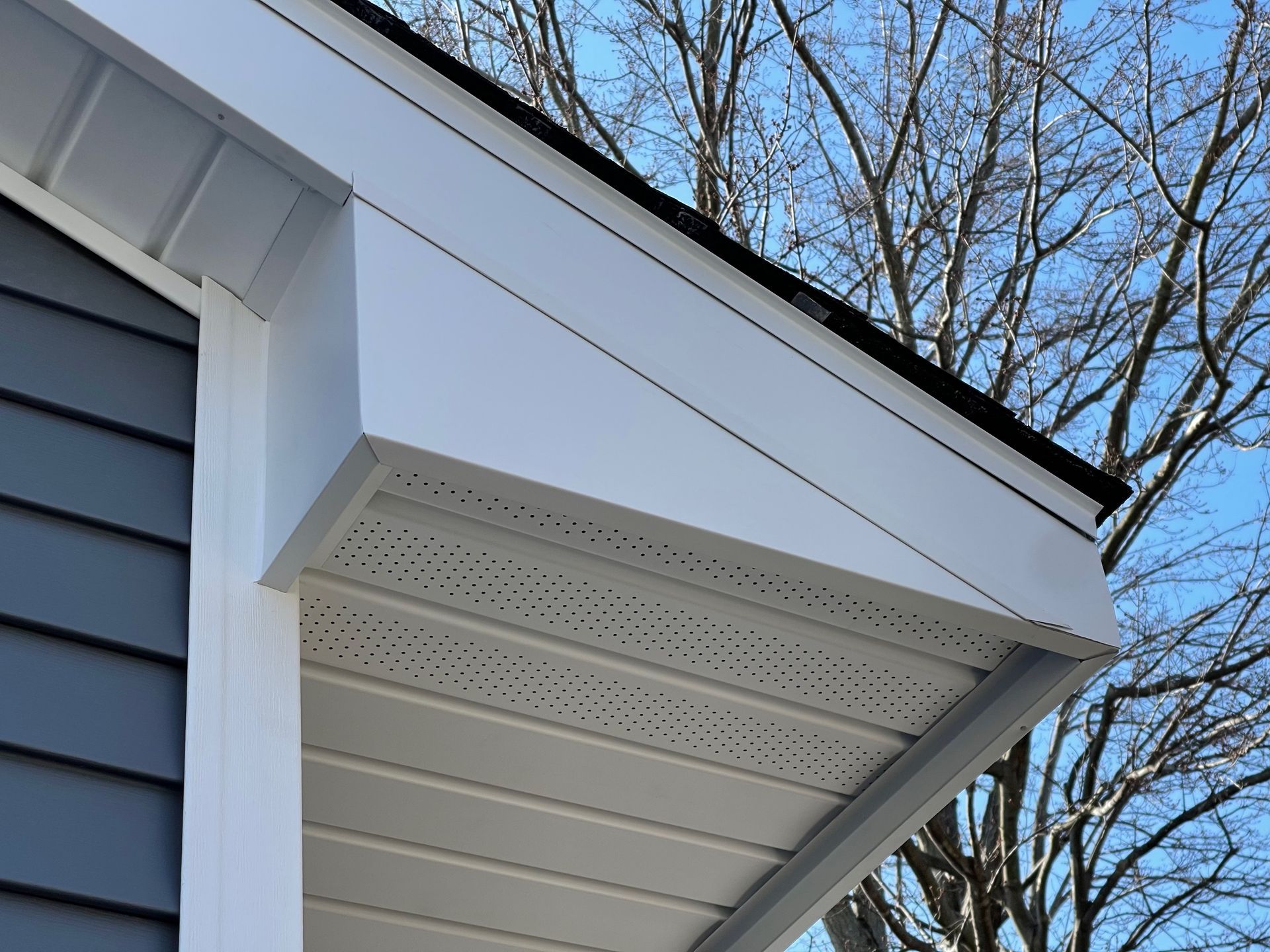 White soffit and trim on a house with gray siding. Perforated underside for ventilation.