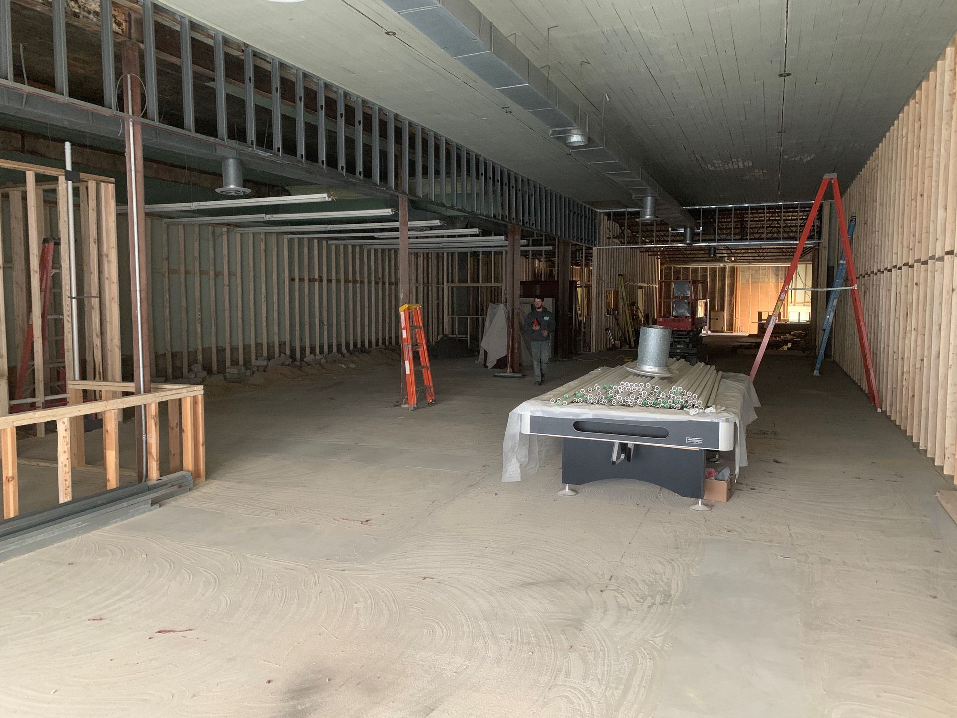 Interior construction site with exposed wood framing, a covered pool table, and ladders.