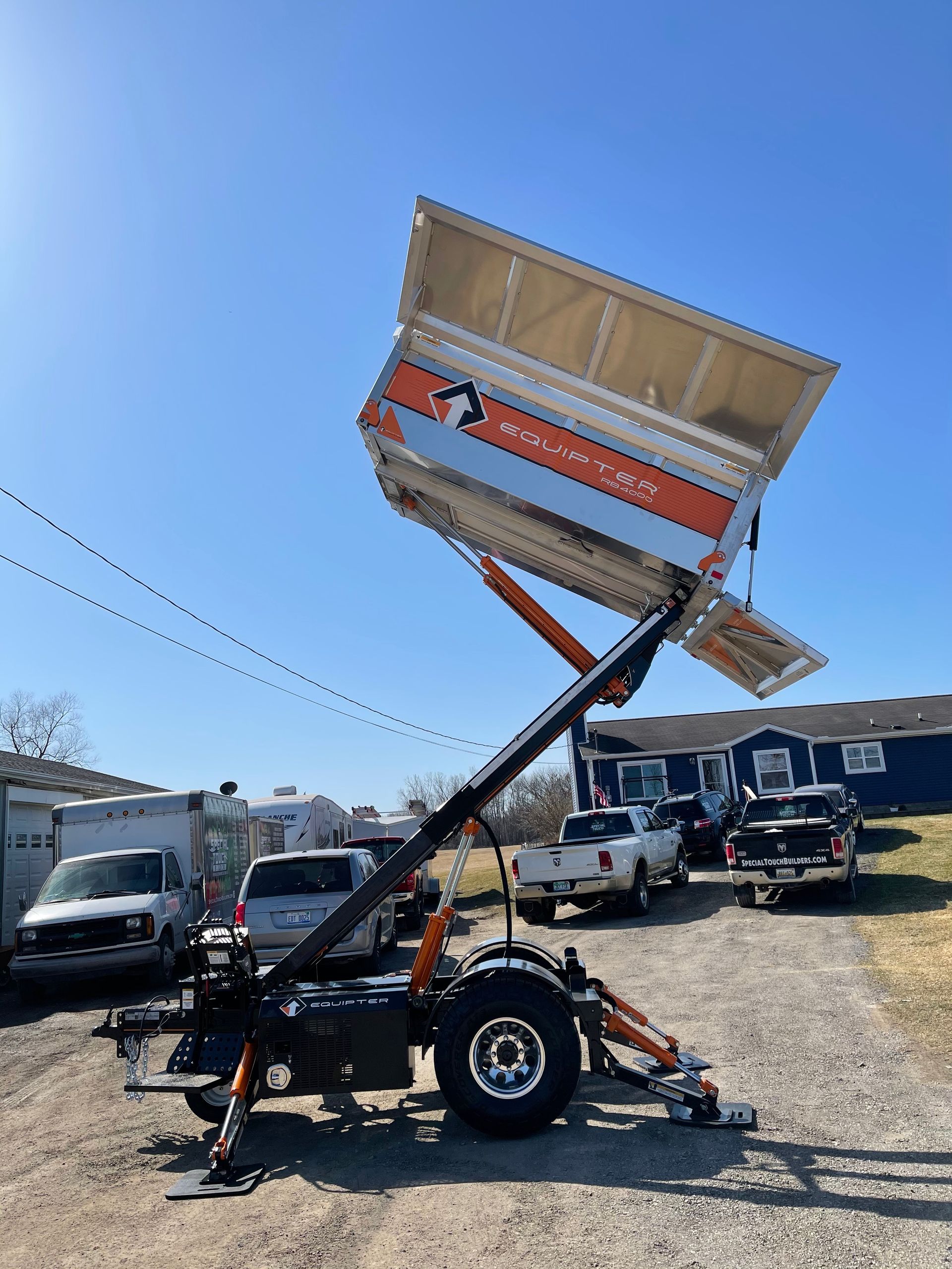 A trailer with a raised dump bed; blue sky and vehicles in the background.