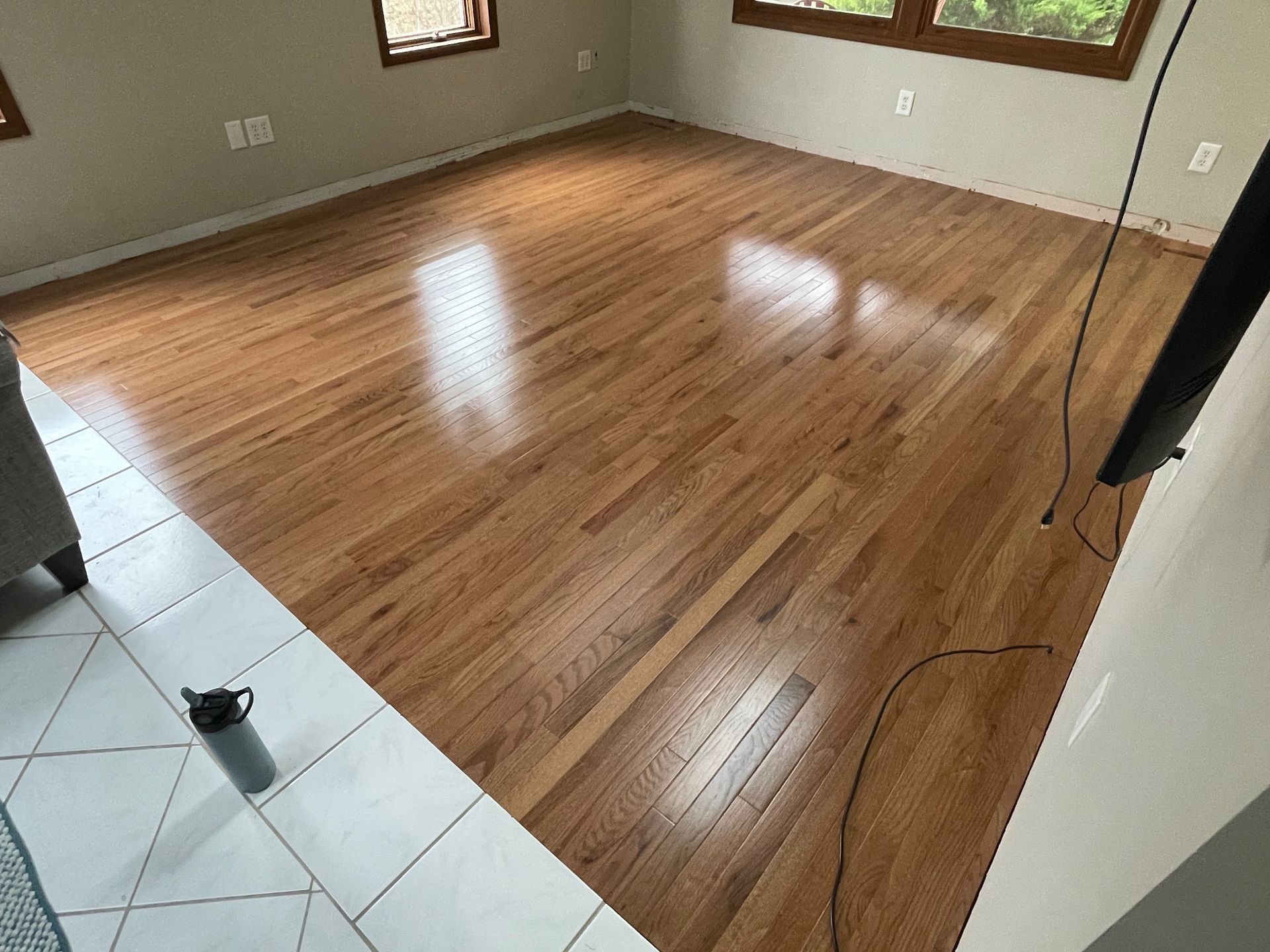 Shiny, wood floor in a room with a white tiled border and window light reflecting.