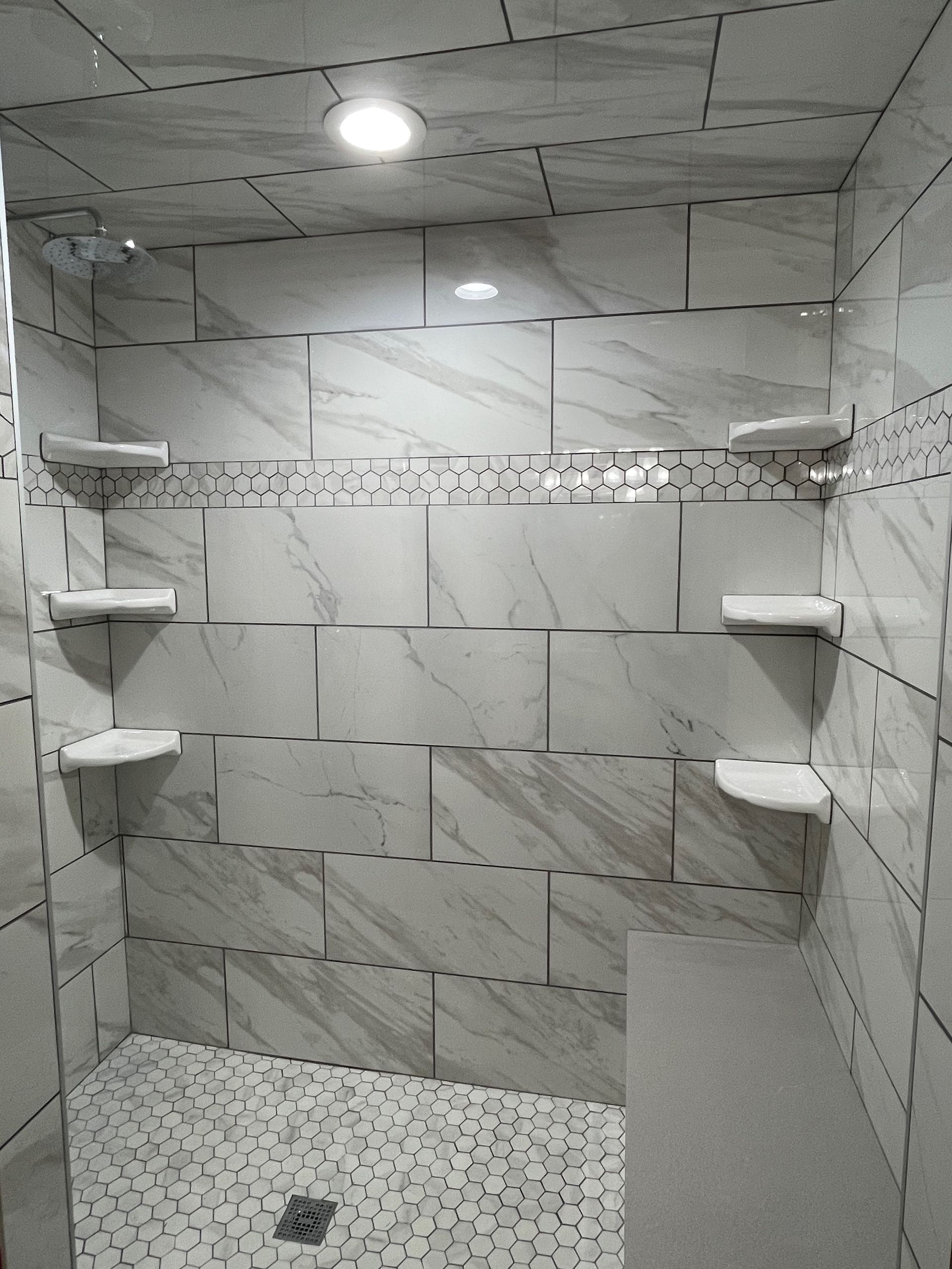 White tiled shower with built-in shelves, pebble floor, and glass showerhead.