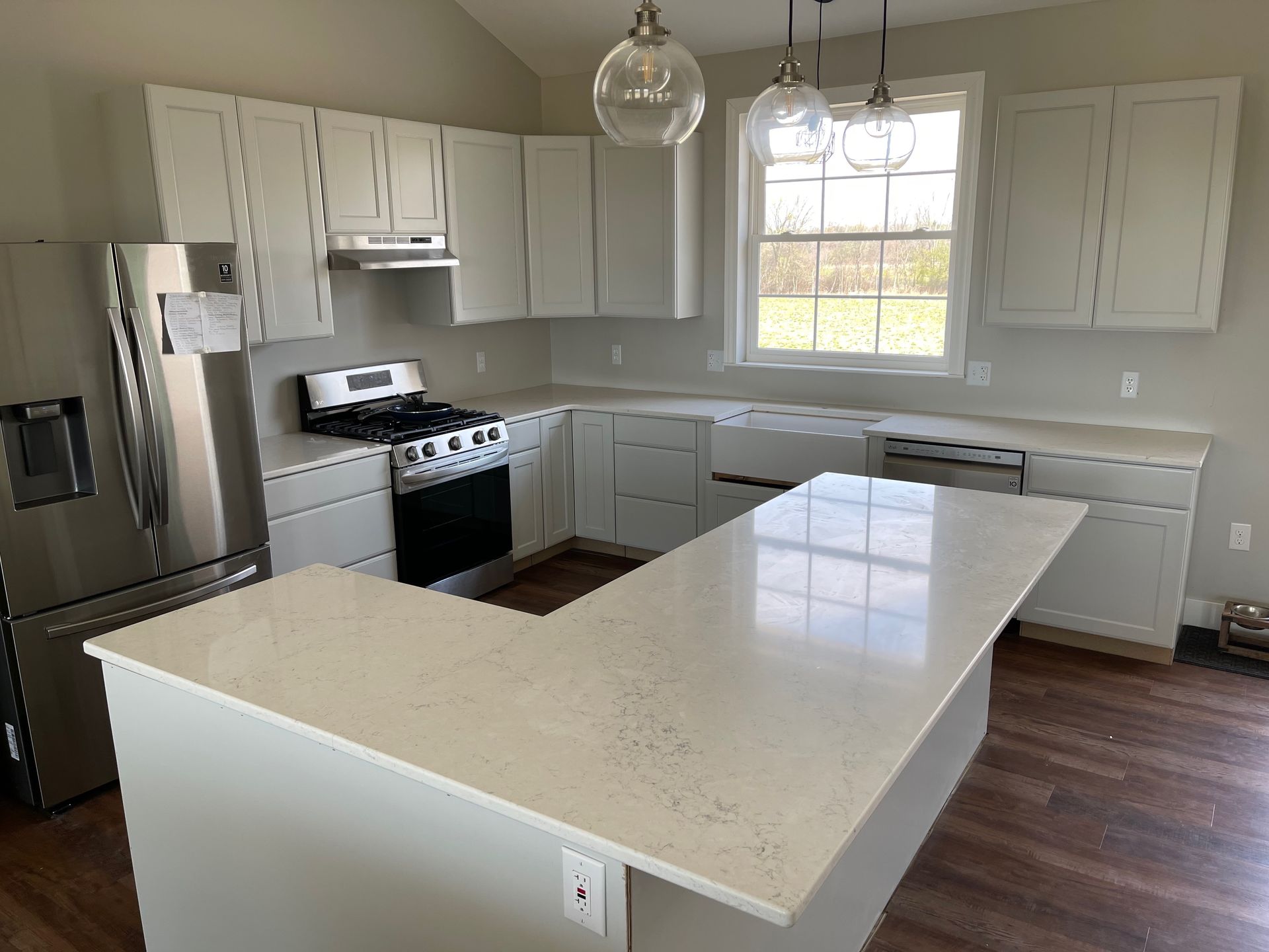 Modern kitchen with light gray cabinets, quartz countertops, stainless steel appliances, and wood floor.