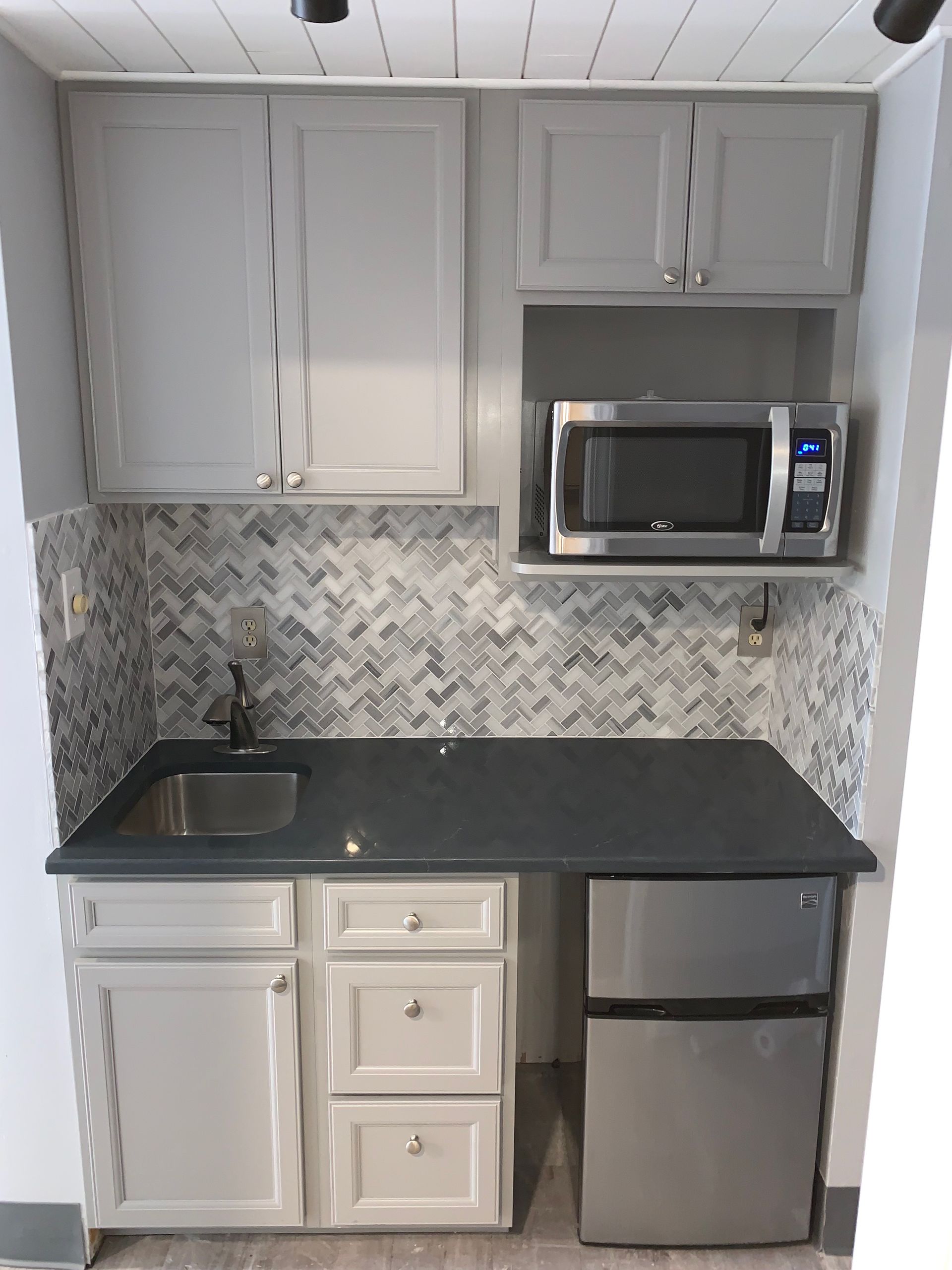 Small kitchen with gray cabinets, microwave, sink, and mini-fridge.