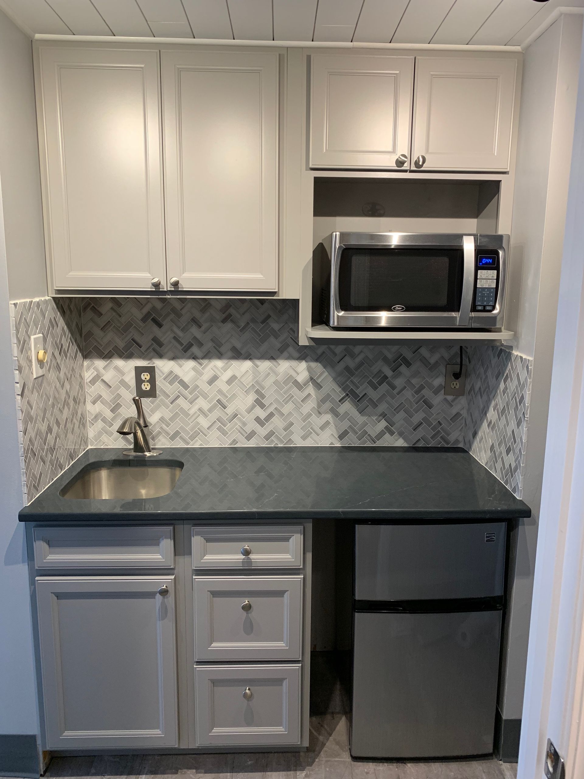Small gray kitchenette with cabinets, sink, microwave, and mini-fridge.