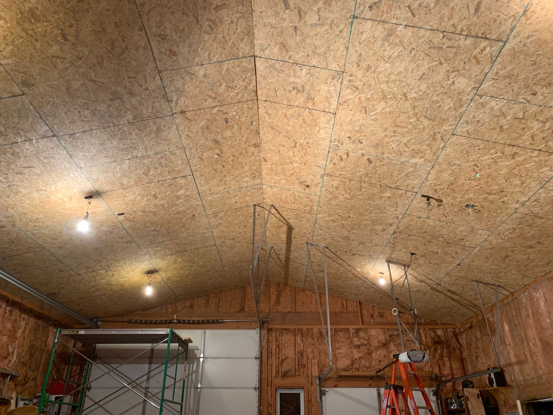 Ceiling with OSB panels, recessed lights, and exposed rafters in a garage setting.